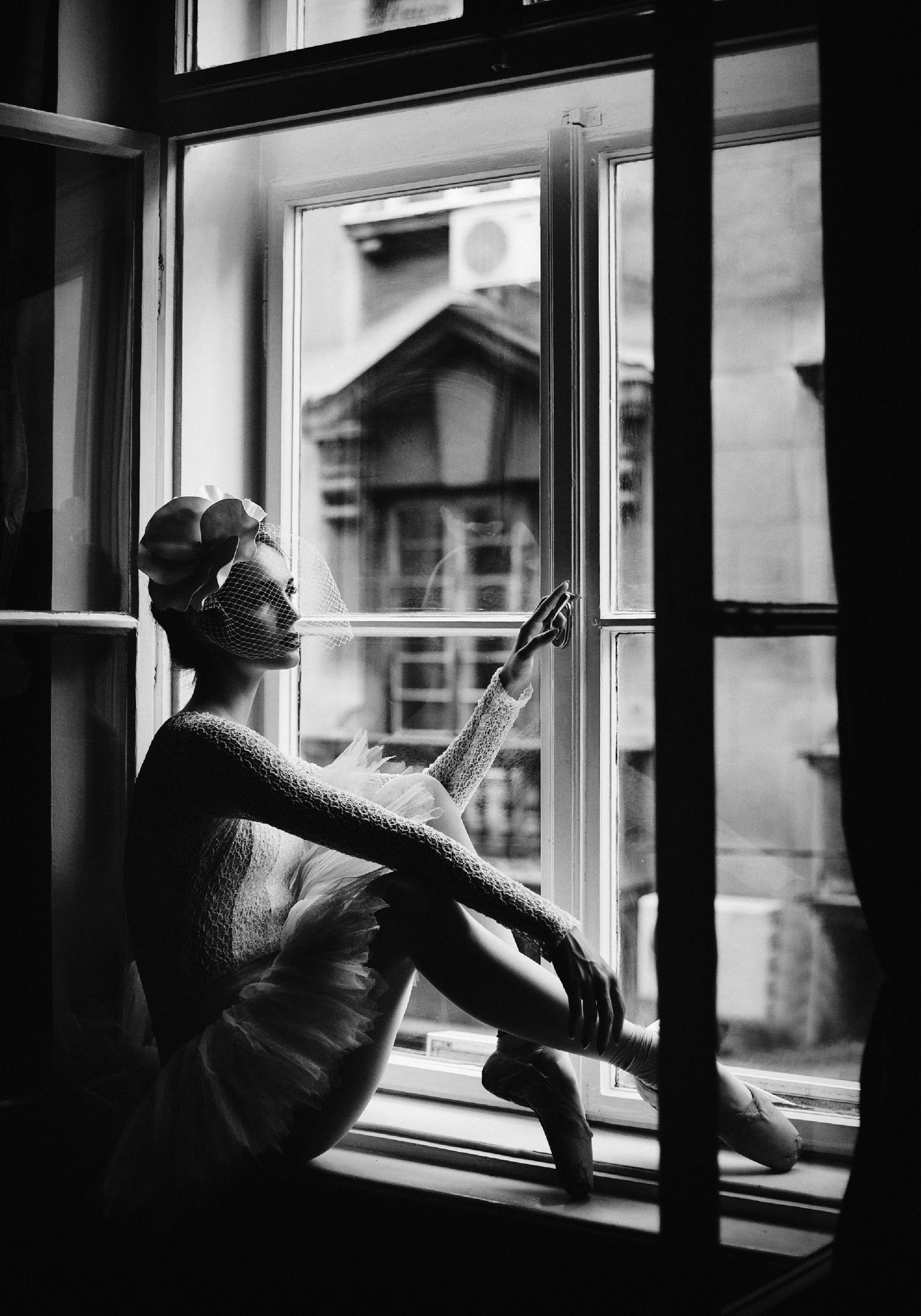 Svartvit fotokonst av en ballerina i fönsterkarm med tyllkjol och dansskor, elegant motiv.