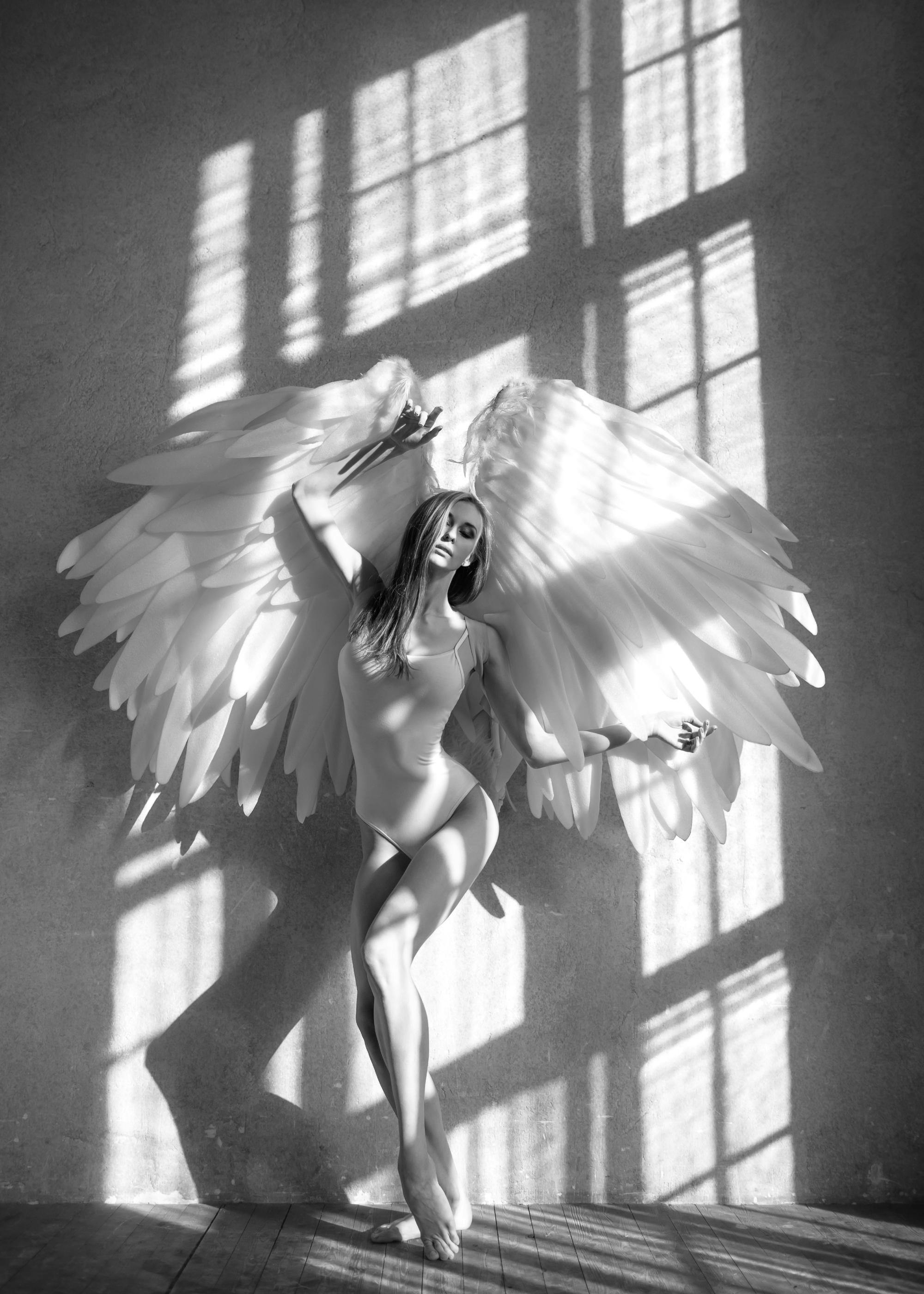 Schwarzweiß-Fotoposter einer Frau mit riesigen Engelsflügeln in einem sonnendurchfluteten Raum mit Schatten.