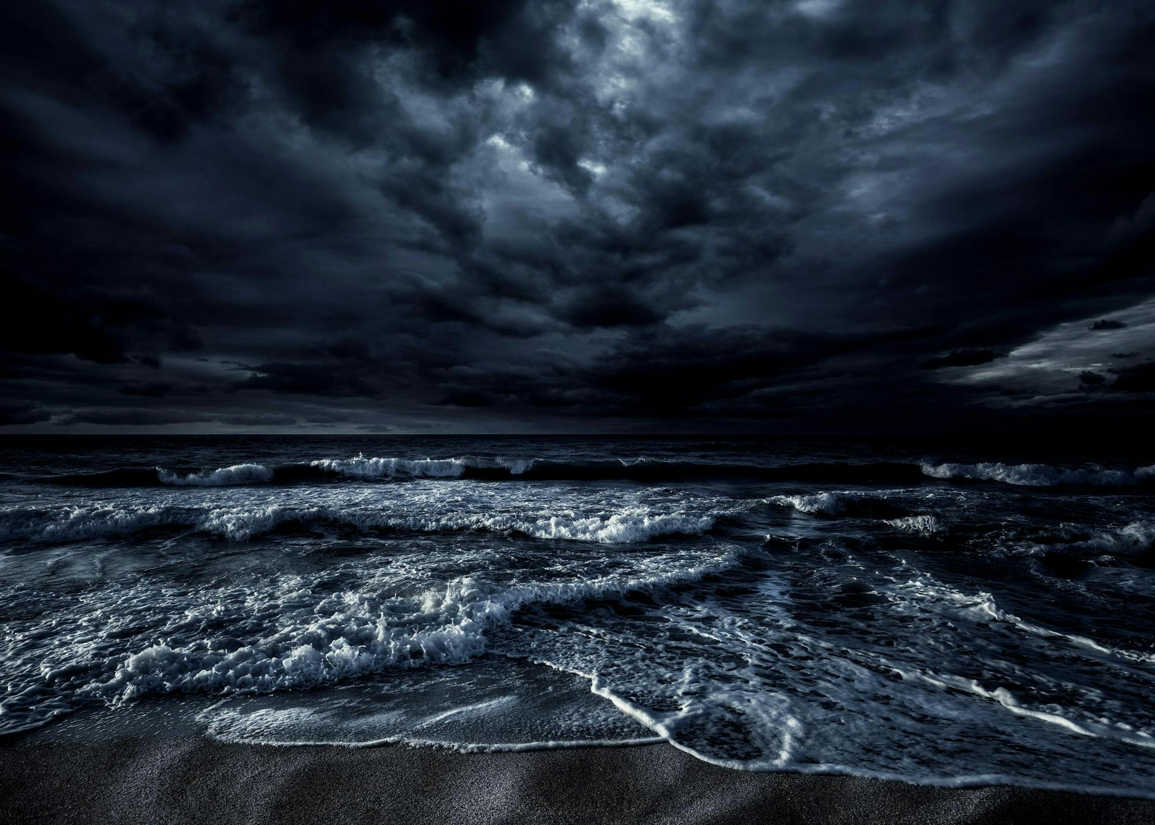 Mørk, stormfull havplakat med hvite bølger som slår inn mot en strand under en dramatisk, overskyet himmel.