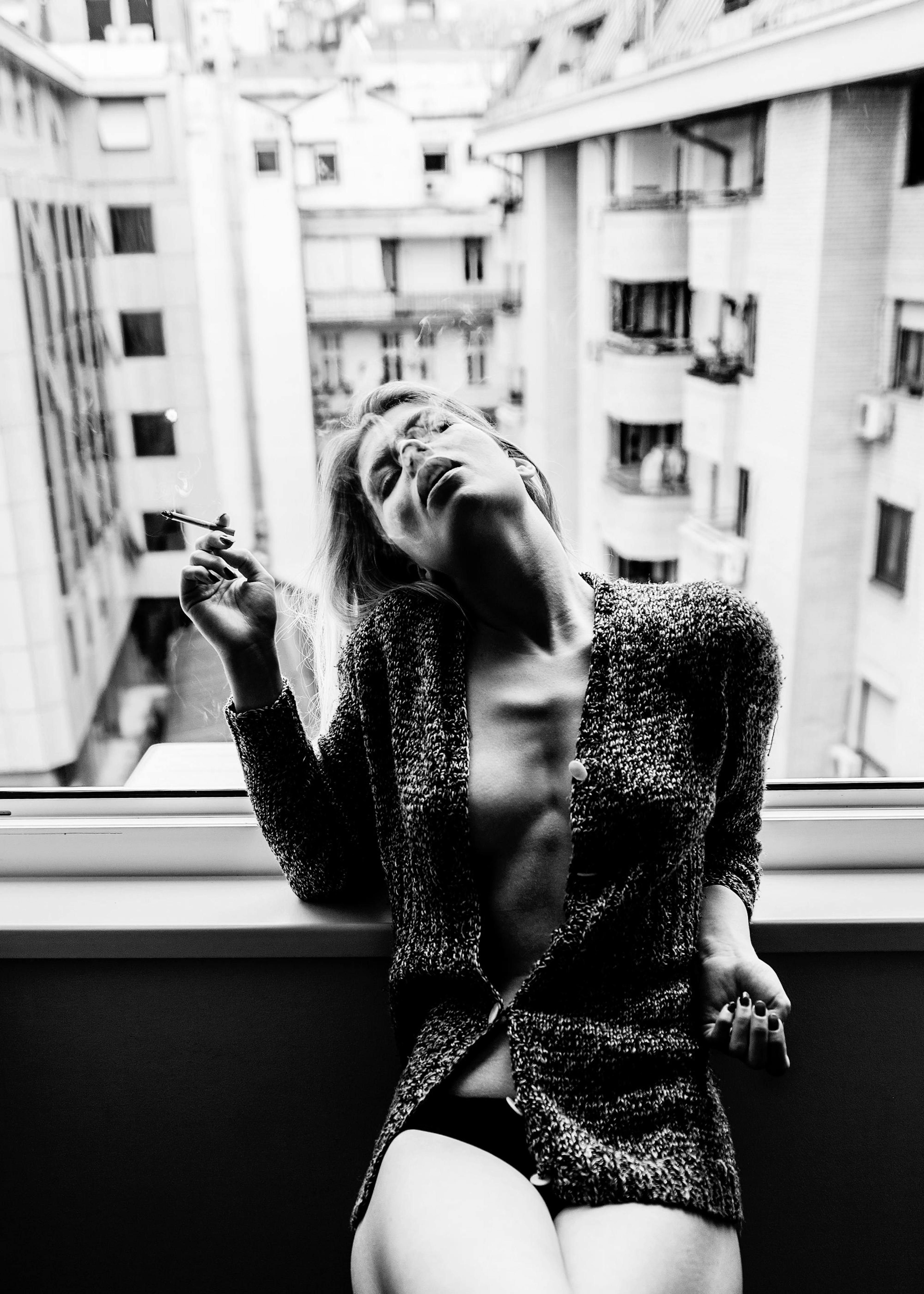 Black and white poster print of a woman smoking by a window, exhaling smoke upwards.