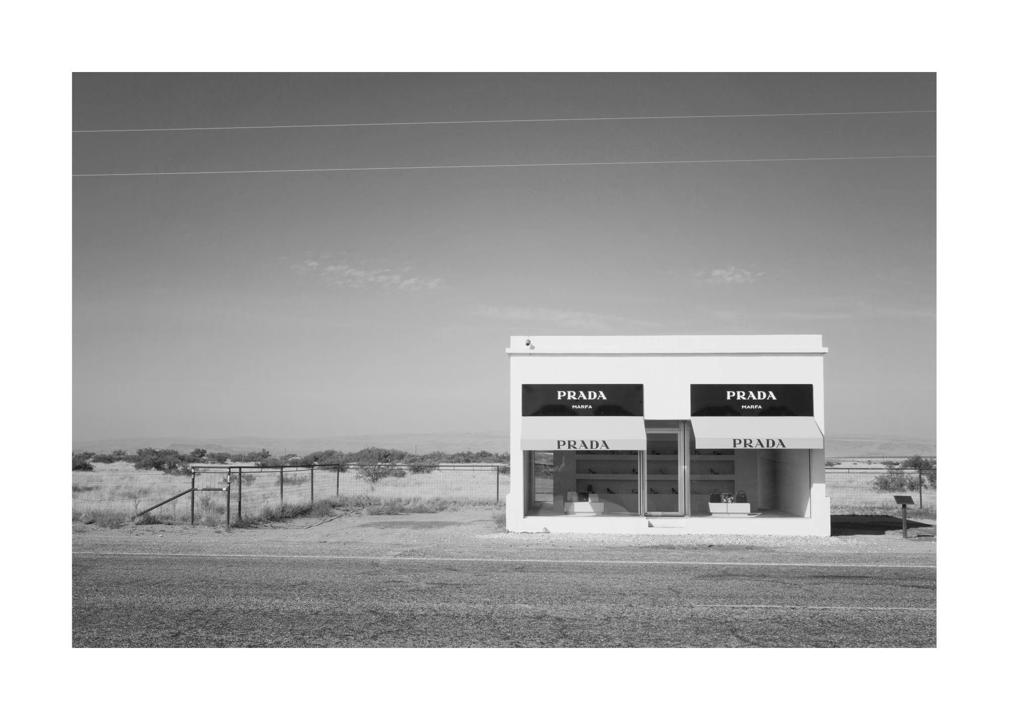 Fotografía en blanco y negro de la tienda Prada Marfa en el desierto de Texas, EE. UU., con un cielo despejado.