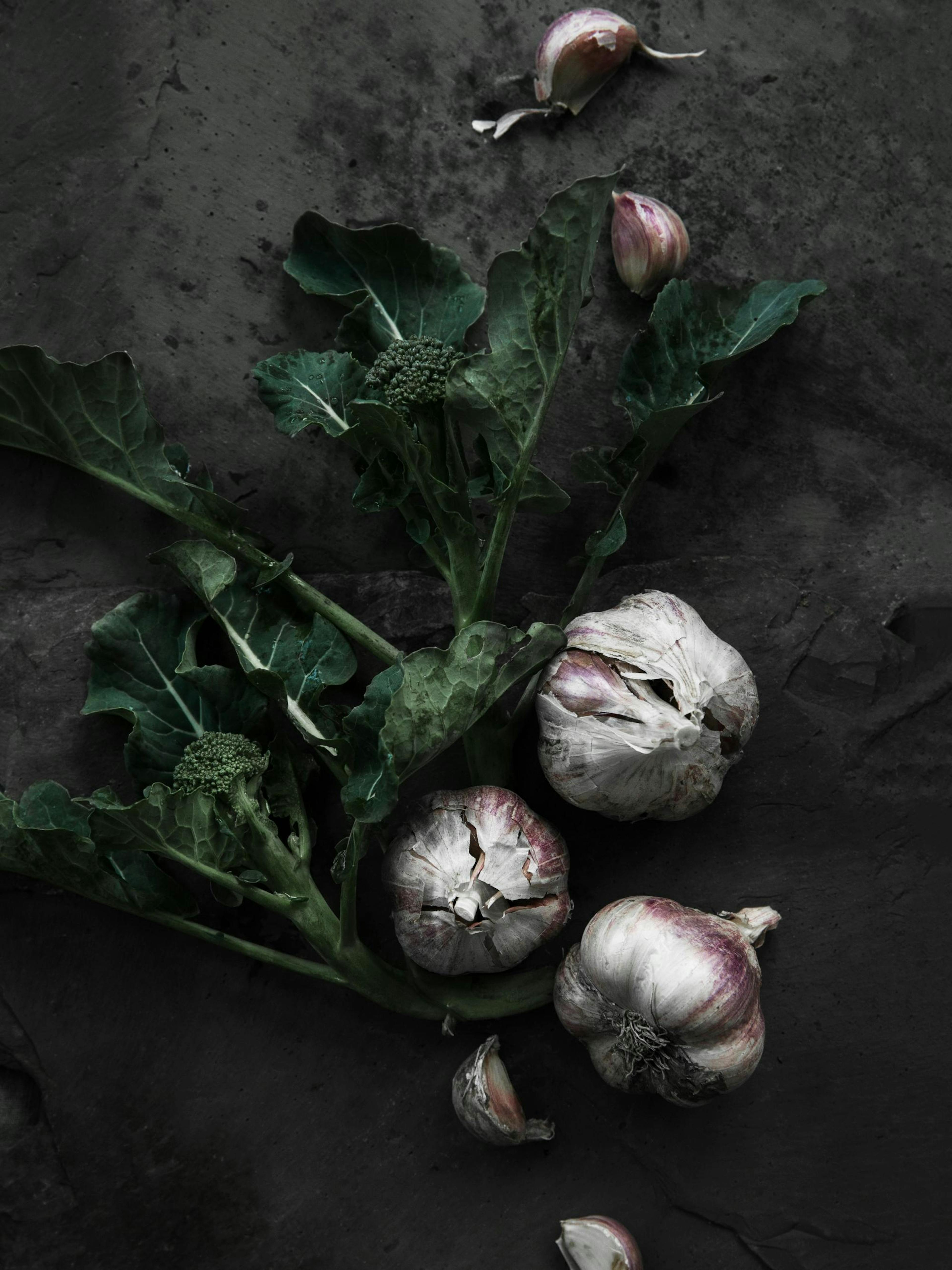 Poster di broccoli e aglio su sfondo scuro, verdure fresche con foglie verdi e bulbi daglio bianchi e viola