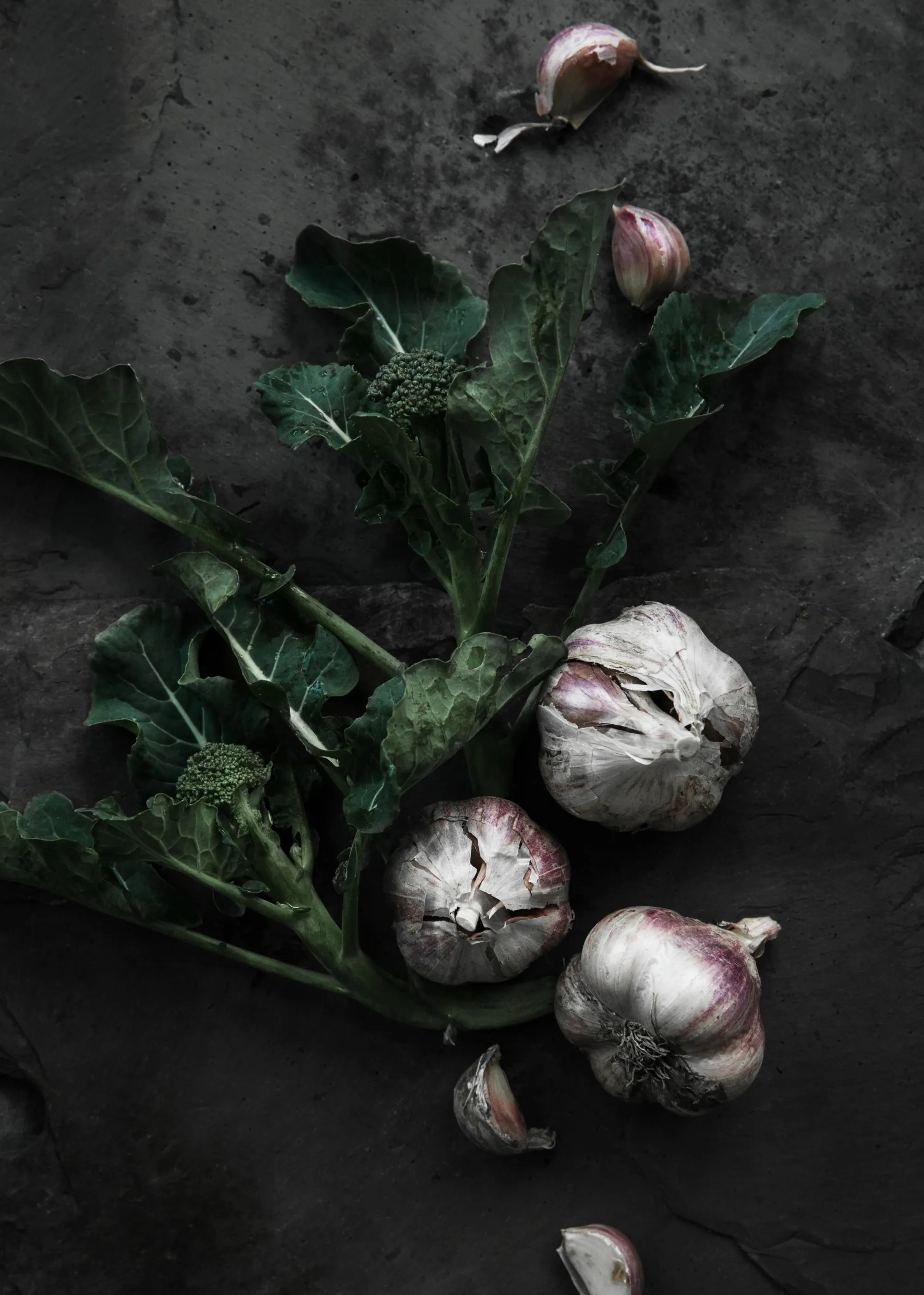 Poster di broccoli e aglio su sfondo scuro, verdure fresche con foglie verdi e bulbi daglio bianchi e viola