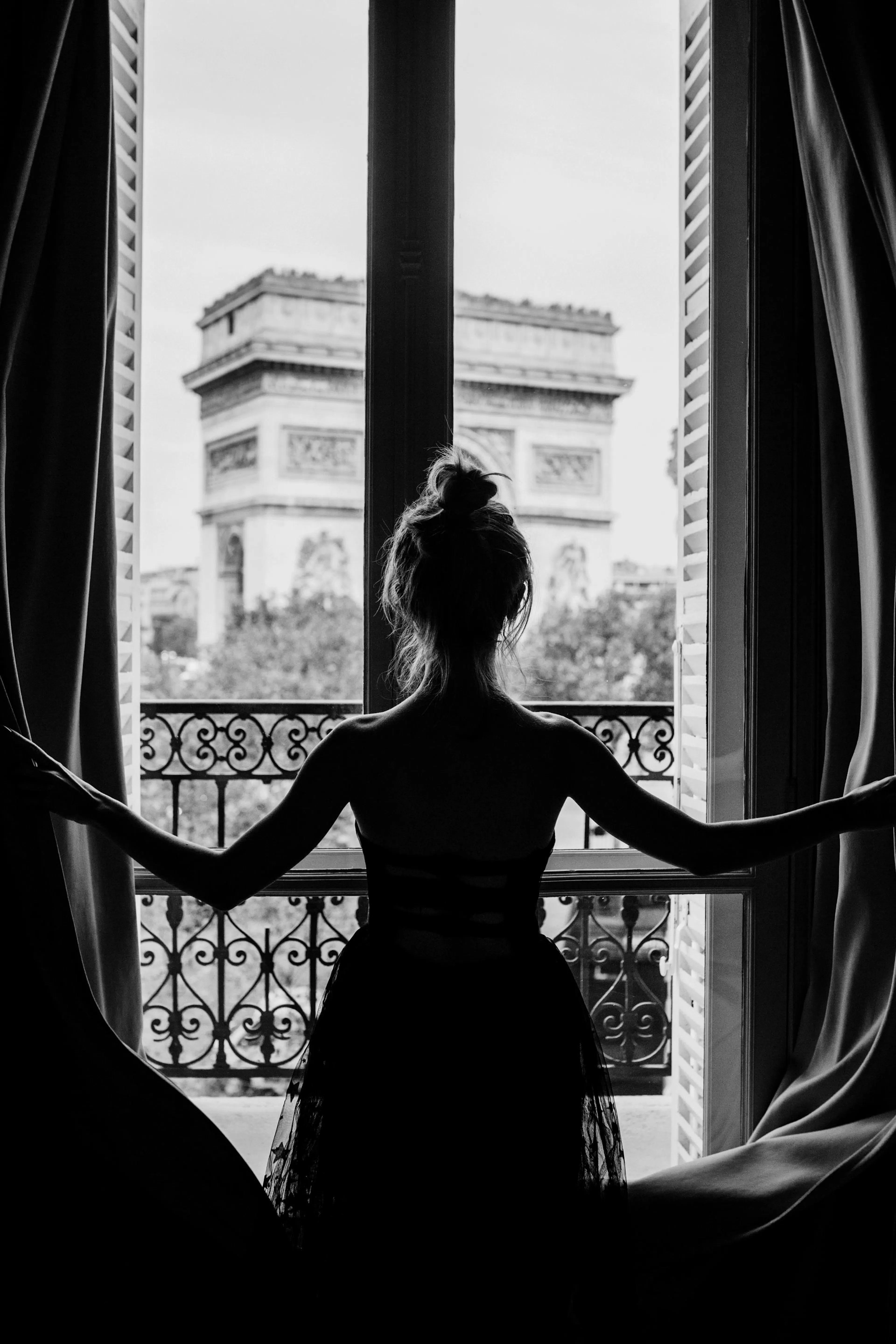 Čiernobiela fotografia ženy v okne s Víťazným oblúkom Paríž.