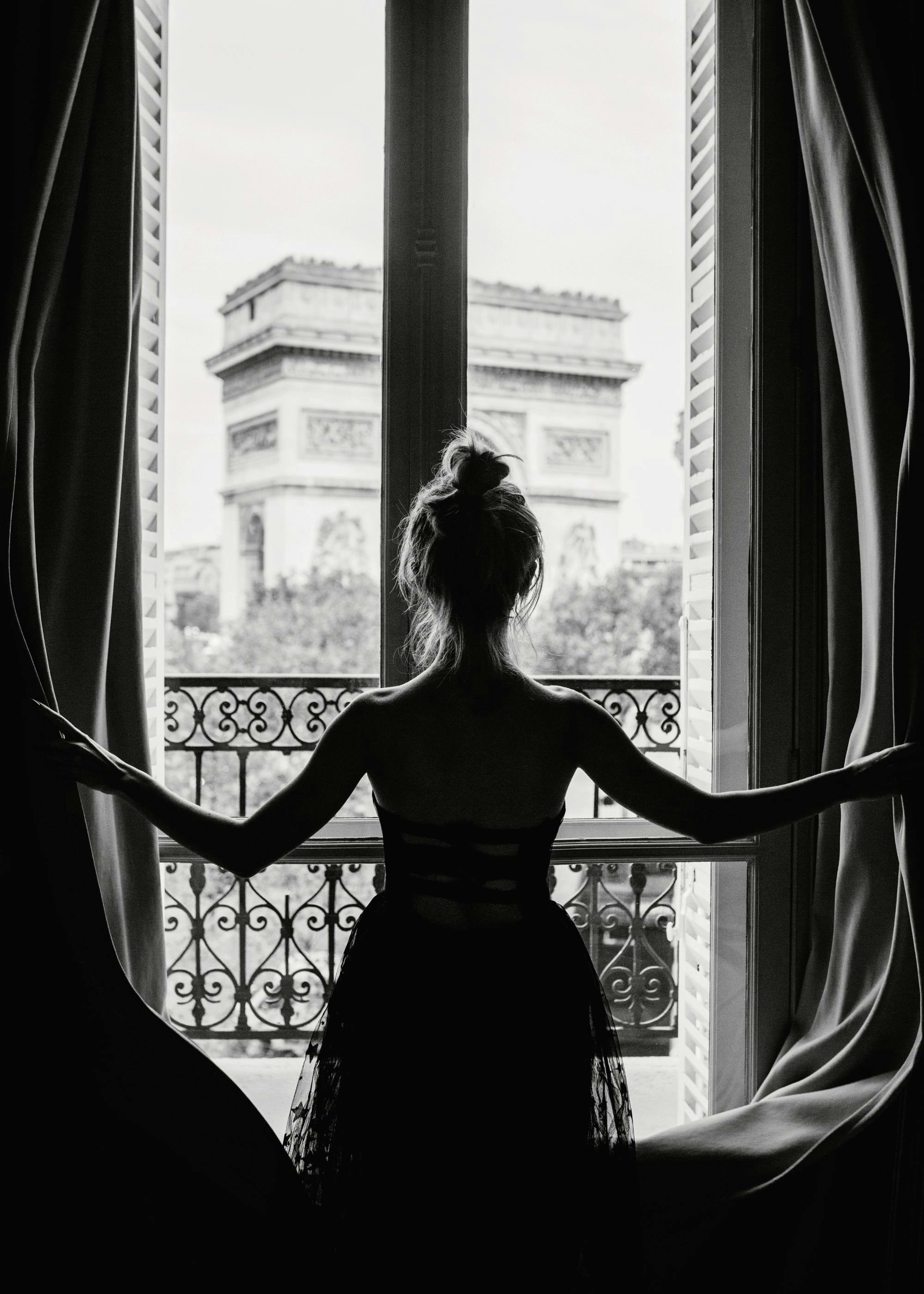 Affiche noir et blanc dune femme devant une fenêtre, regardant lArc de Triomphe, typographie photographique.