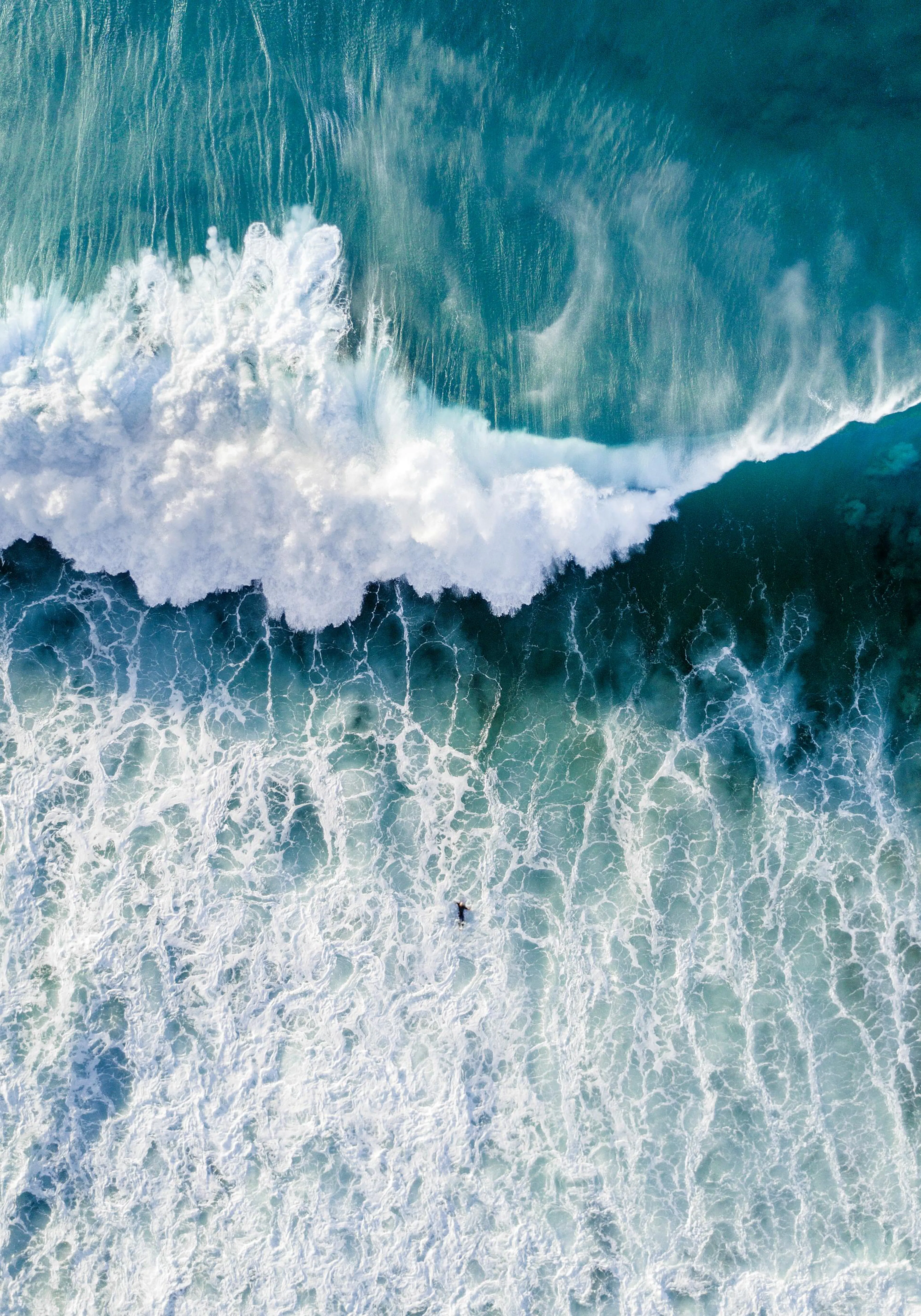 Luchtfoto van surfer in oceaan met turquoise water en witte schuimende golven.