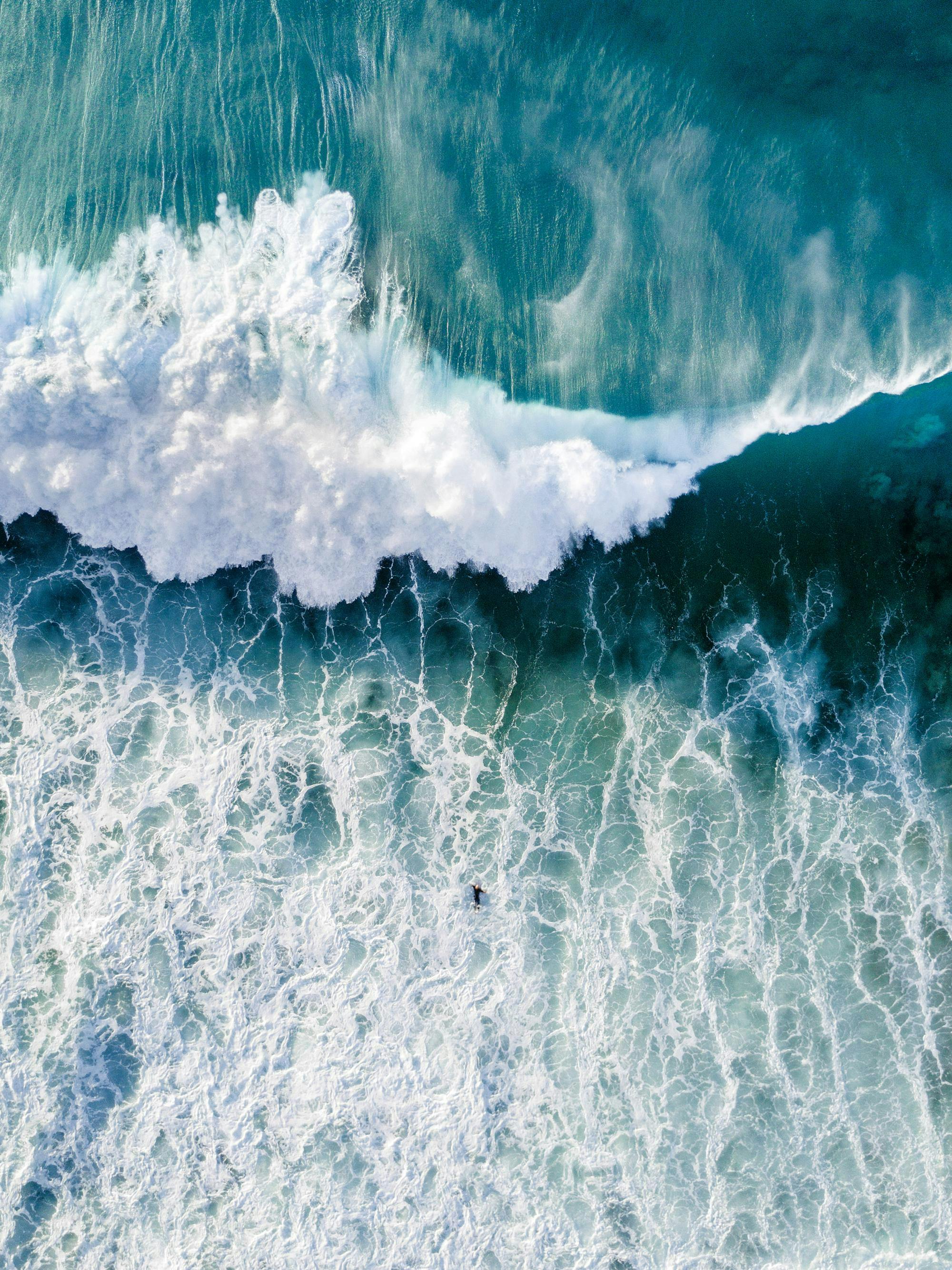 Flygfoto av en surfare i turkost hav med en stor våg som bryter vit skum
