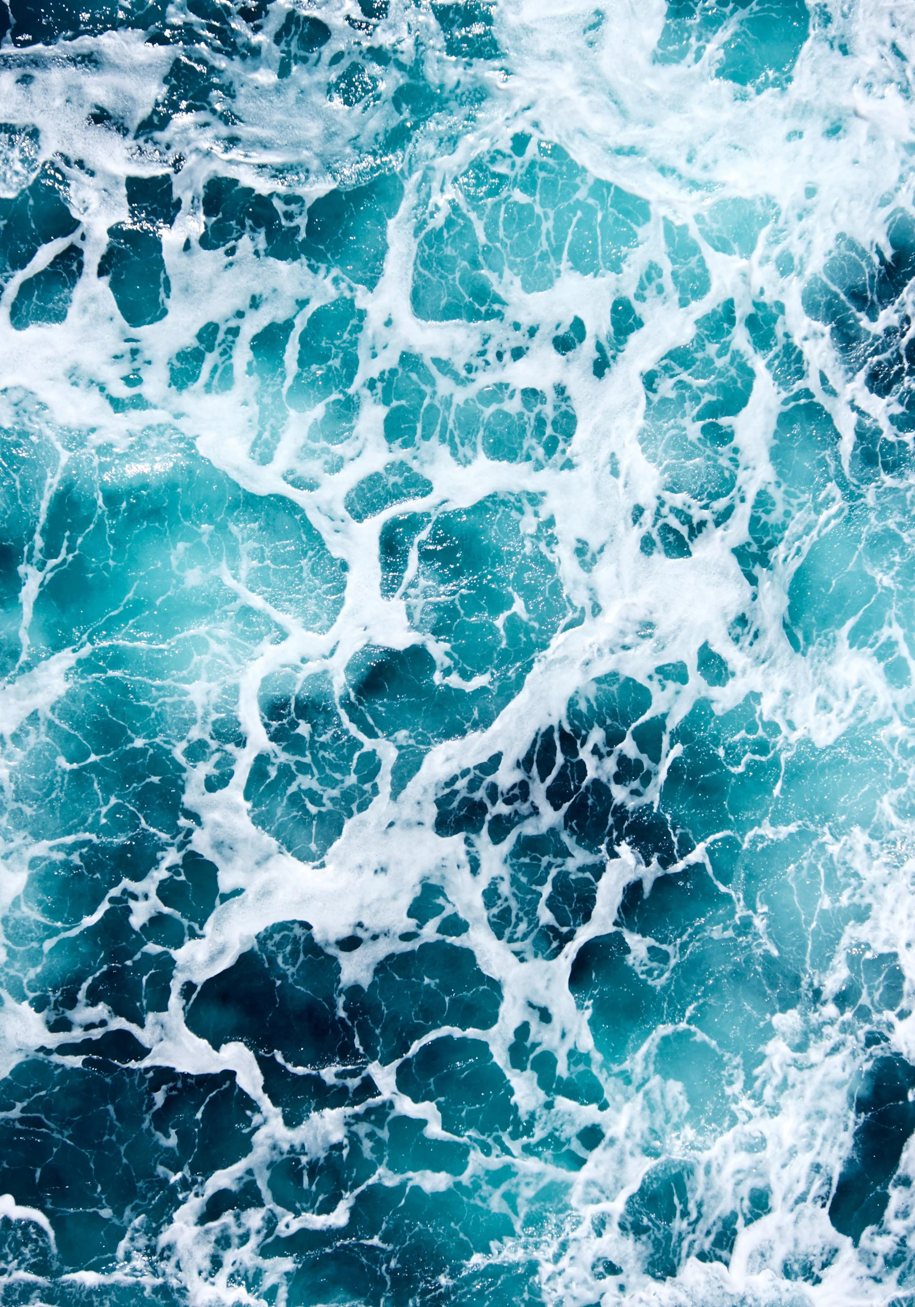 Close-up photo of swirling ocean water with white sea foam over deep turquoise and teal hues.