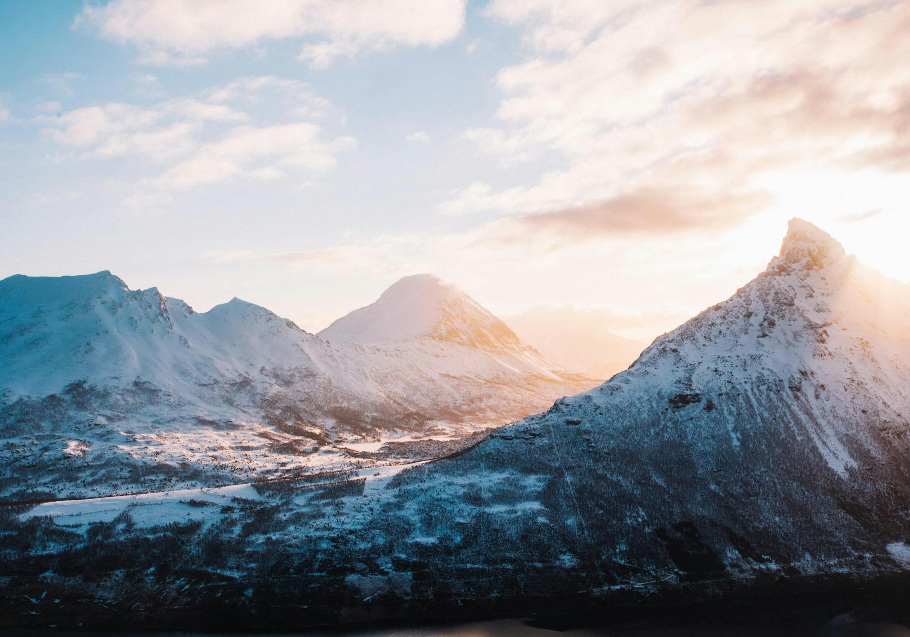 A print of snowy mountains with a sunrise glow, hanging above a white console table with decorative vases and candles.