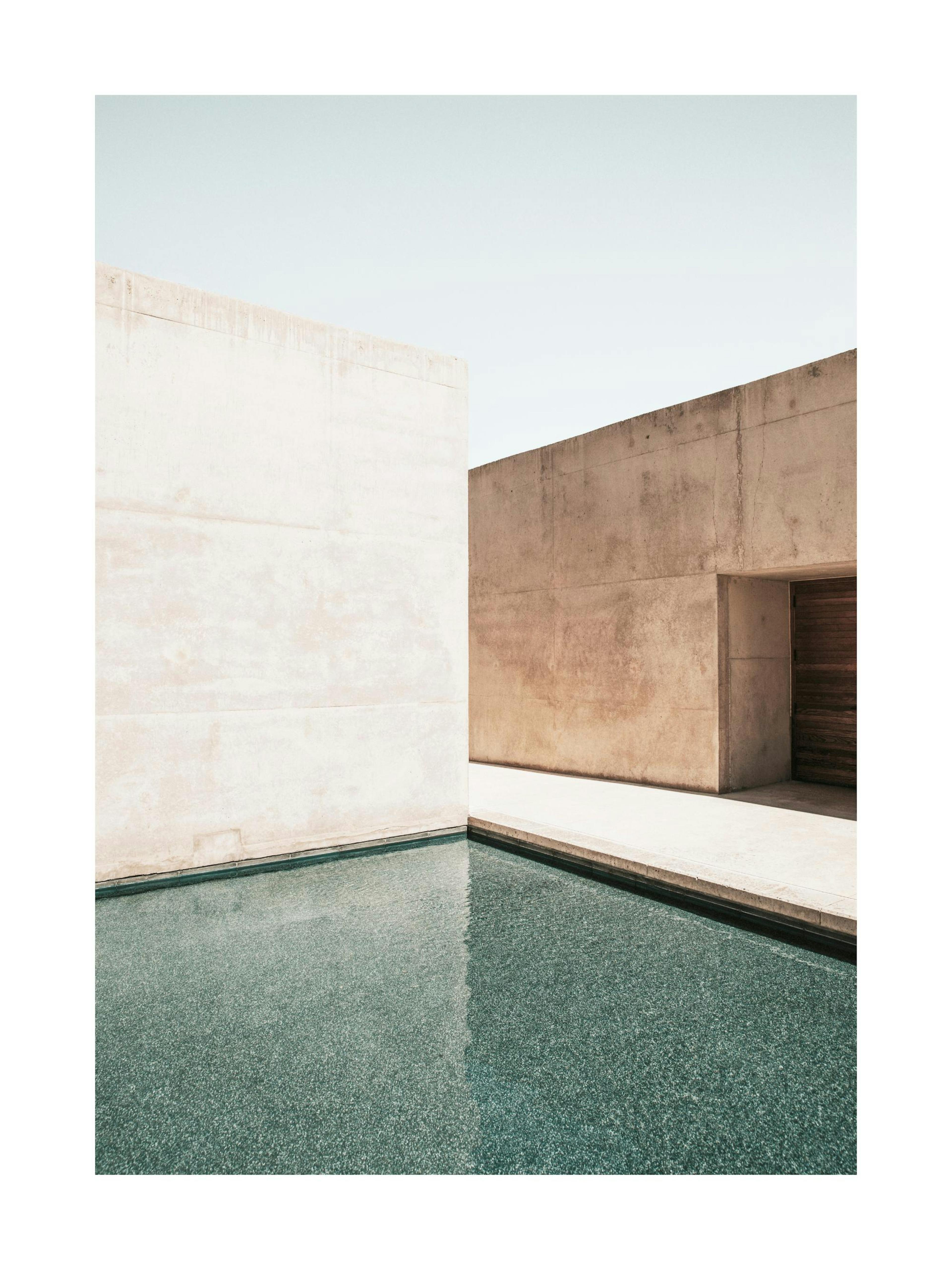 Photograph of concrete building facades and a pool with light blue sky, minimalist architecture poster