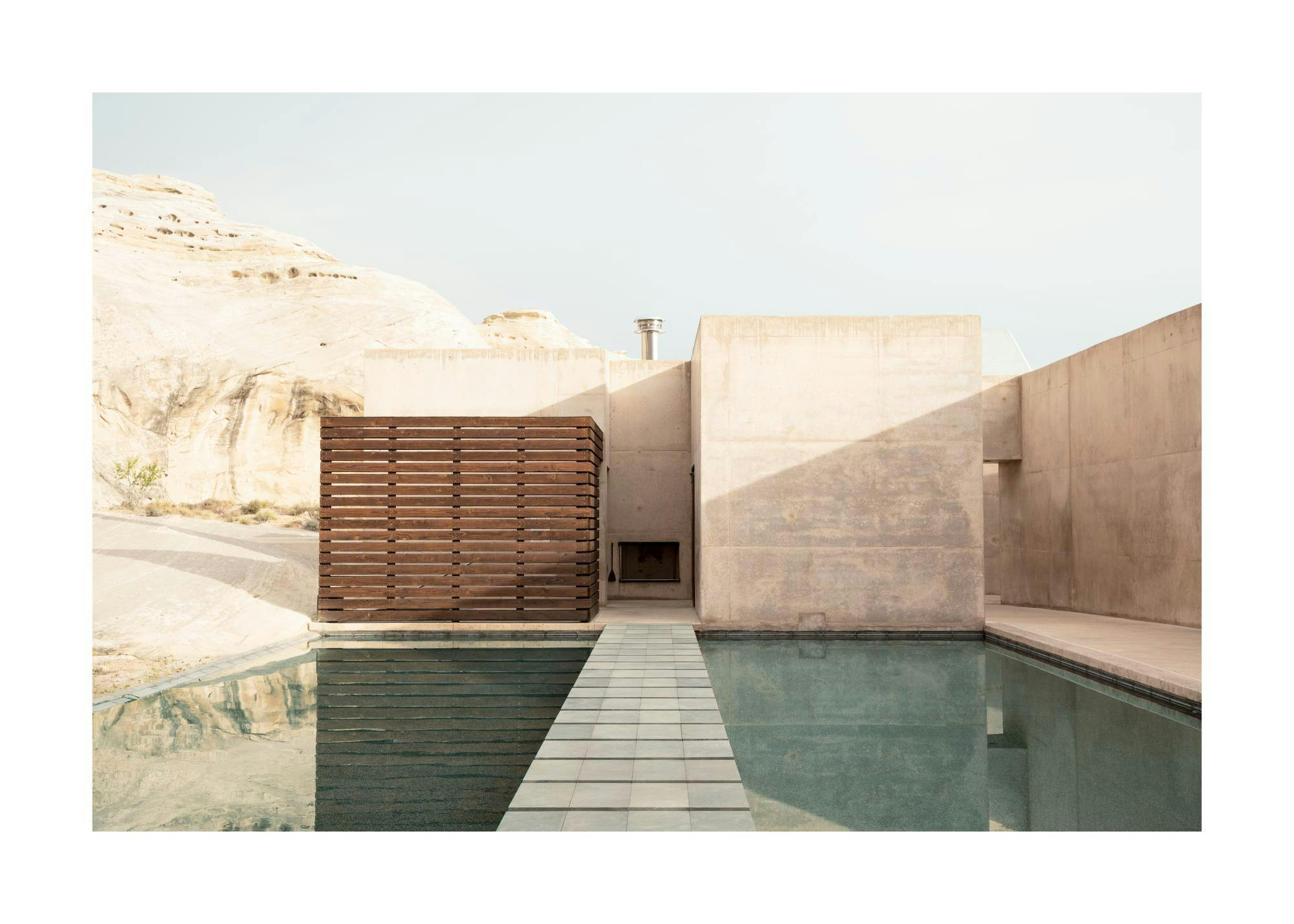 Affiche dune piscine avec un pont au milieu, un bâtiment en béton et des montagnes en arrière-plan. Photographie architecturale.