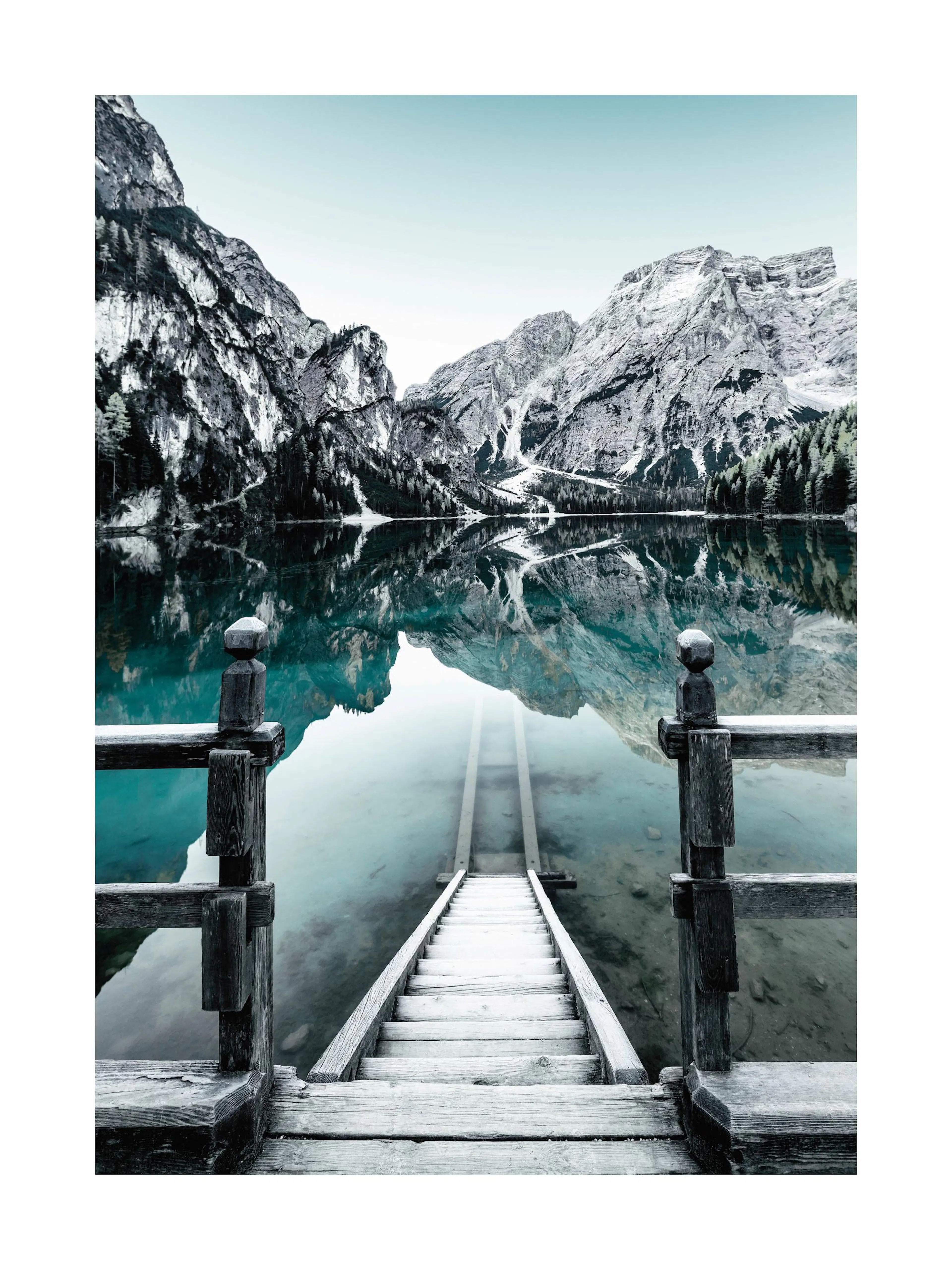 Naturfotografie: verschneite Berge und ruhiger Pragser Wildsee mit Steg in Italien, Spiegelung im klaren Wasser