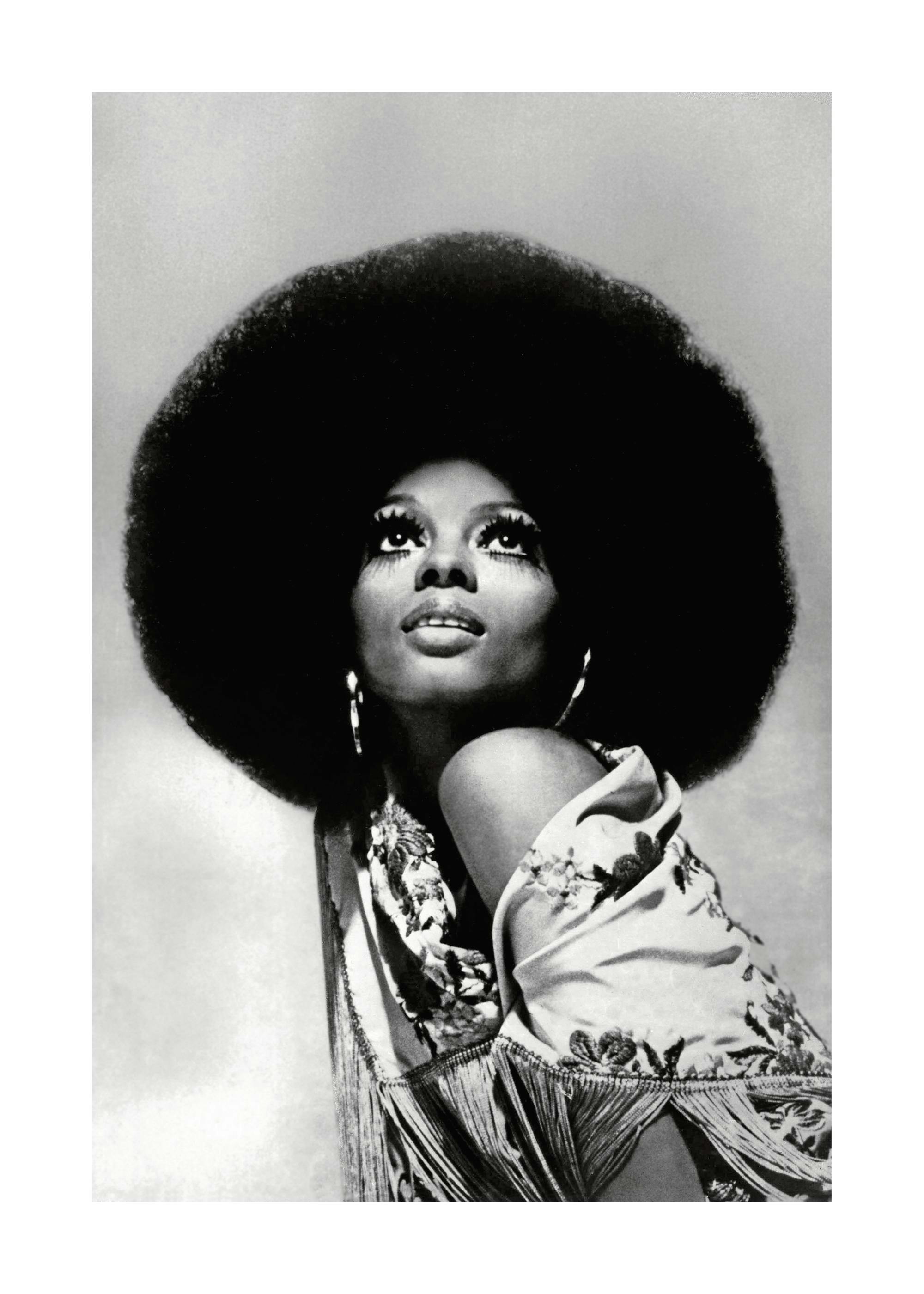 Čiernobiela fotografia Diany Ross s afro účesom, hľadiacej hore, s výraznými mihalnicami a náušnicami.