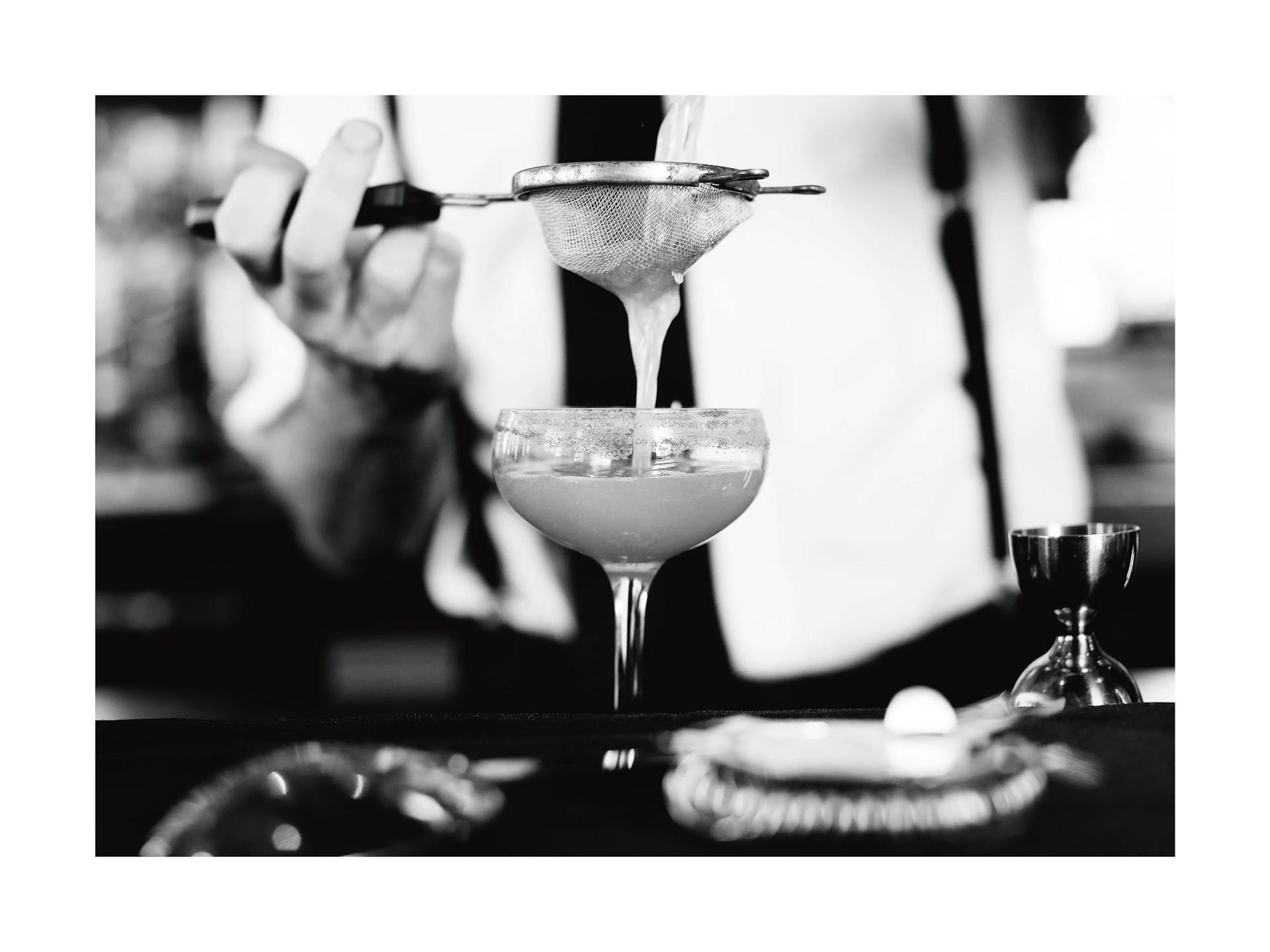 Póster de mixología en blanco y negro, un barman sirviendo un cóctel a través de un colador, bebida vintage.