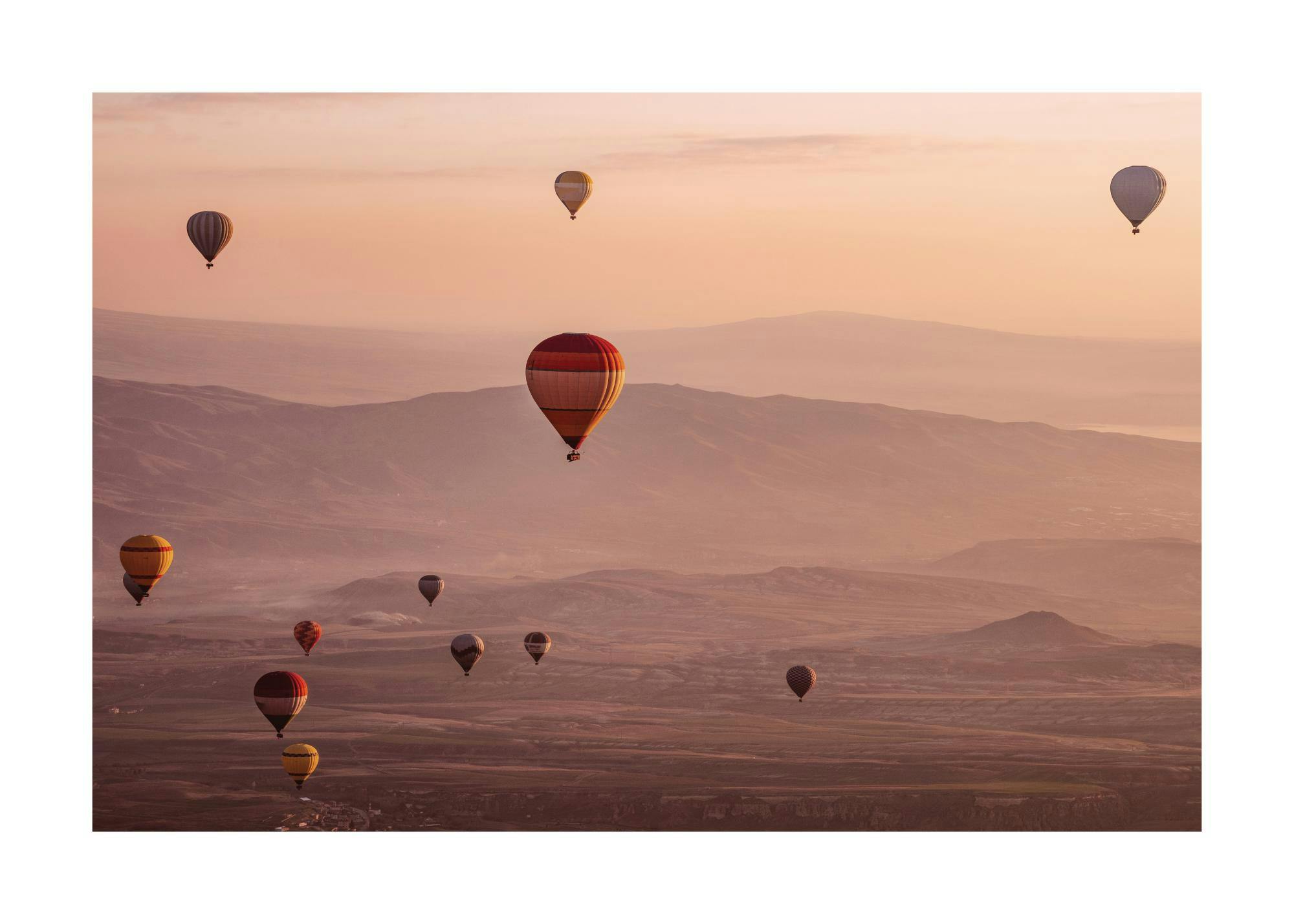 Affiche de montgolfières multicolores flottant au-dessus dun paysage montagneux au lever du soleil avec des teintes roses et ora