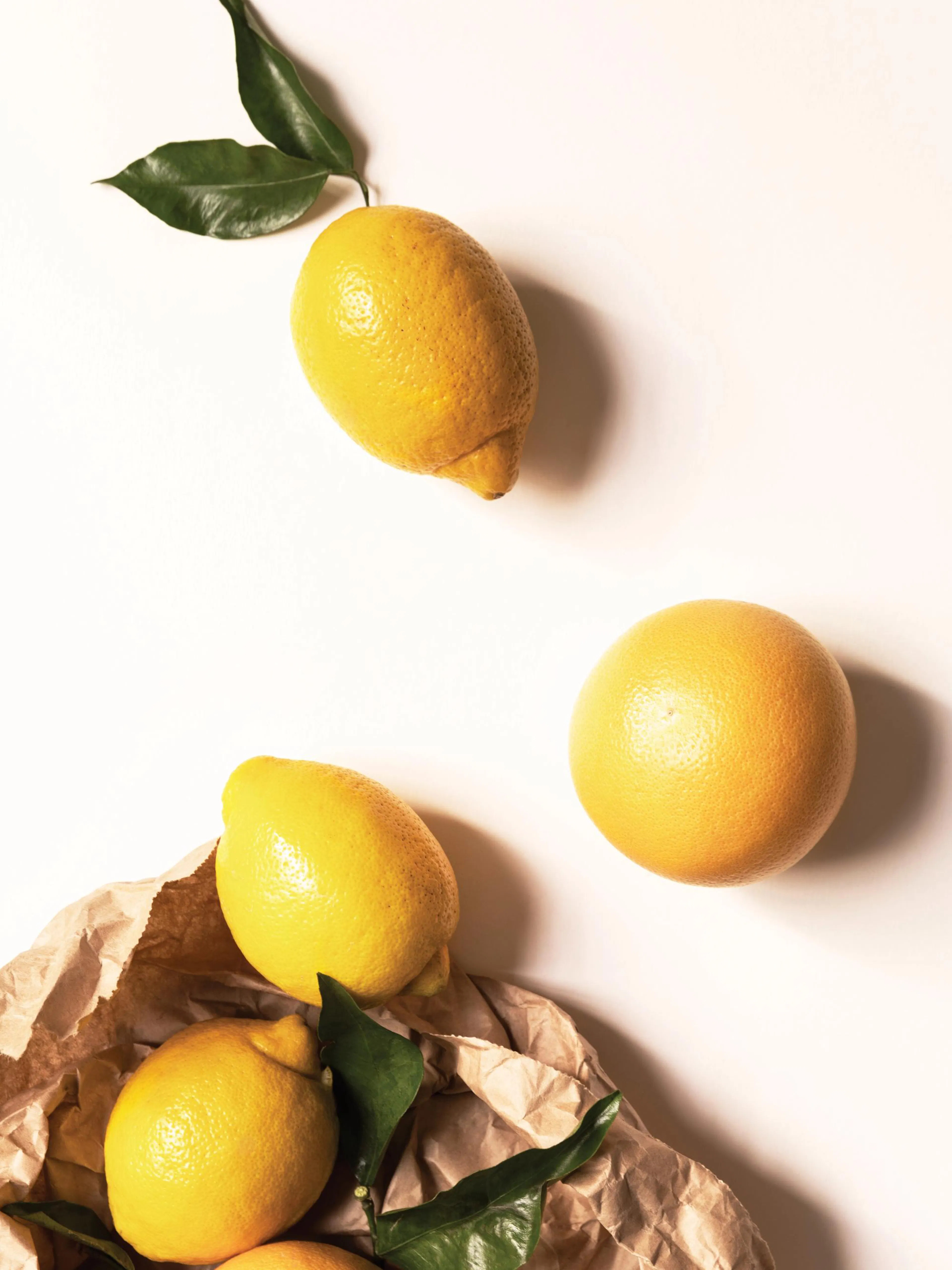 Póster con limones amarillos y hojas verdes en una bolsa de papel marrón sobre un fondo beige claro, estilo fotografía de frutas