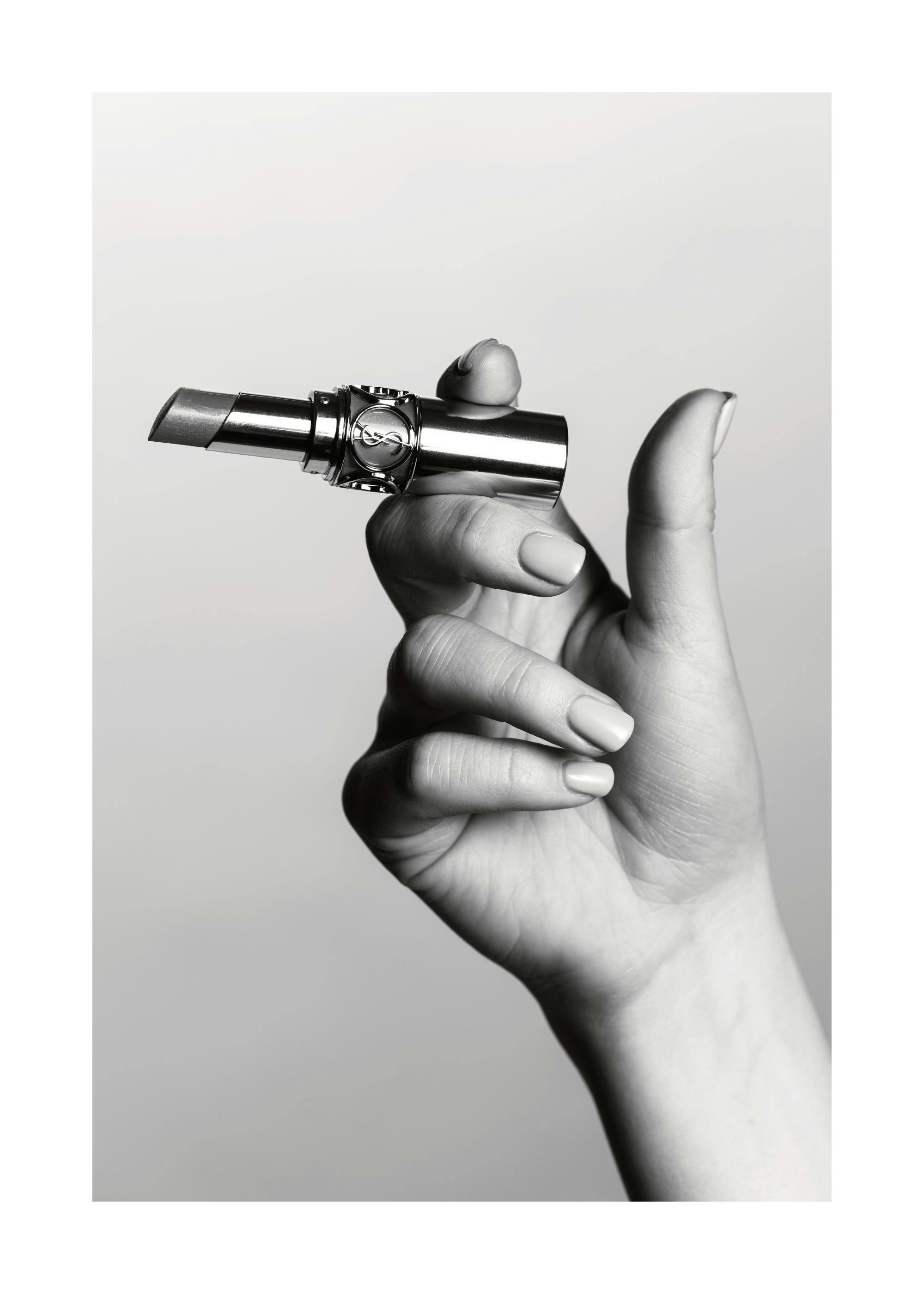 Black and white fashion print of a hand holding a YSL lipstick like a cigarette, a stylish beauty poster.