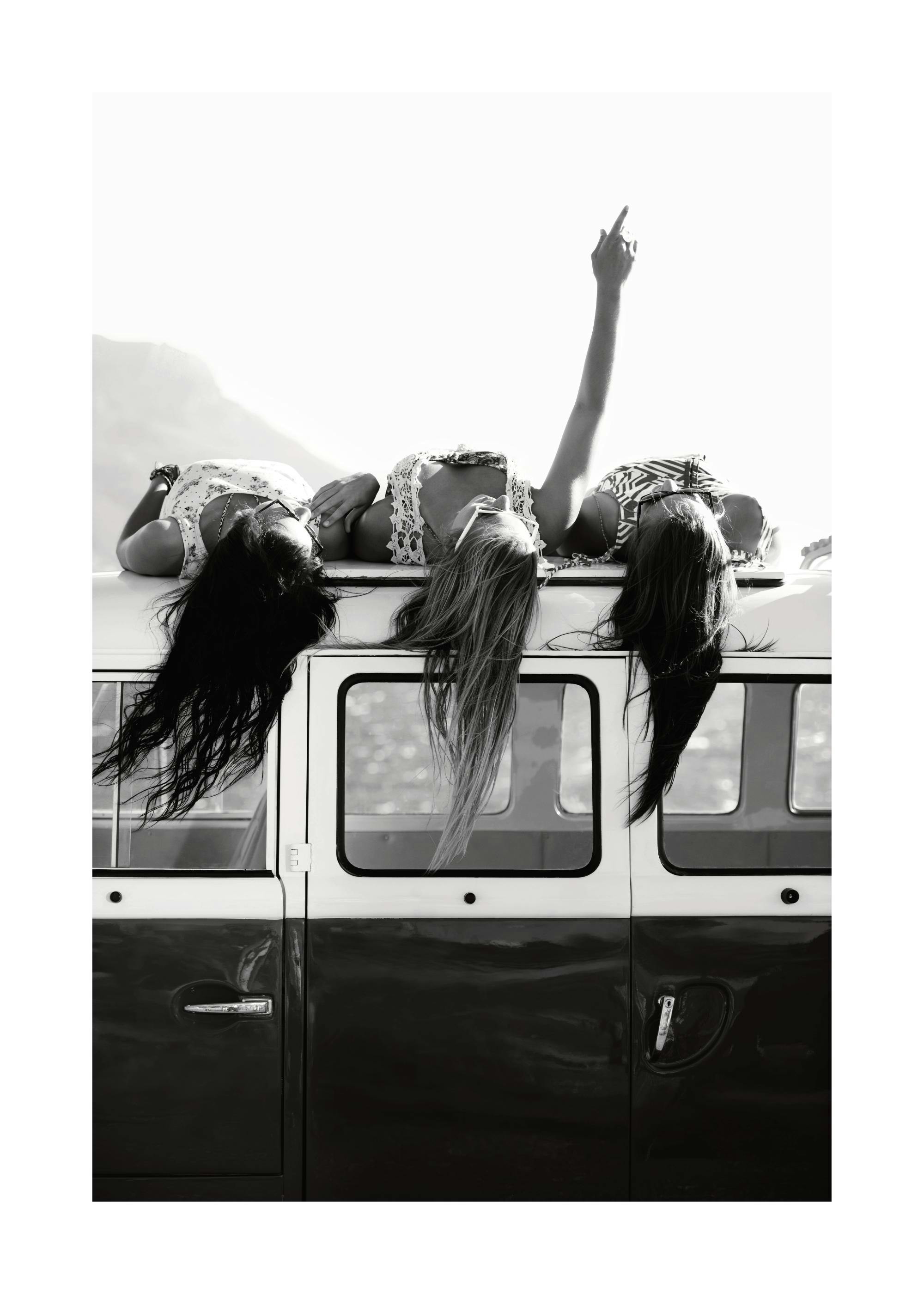 Póster a preto e branco: três raparigas deitadas no tejadilho de uma carrinha. Fotografia de amigos, roadtrip.