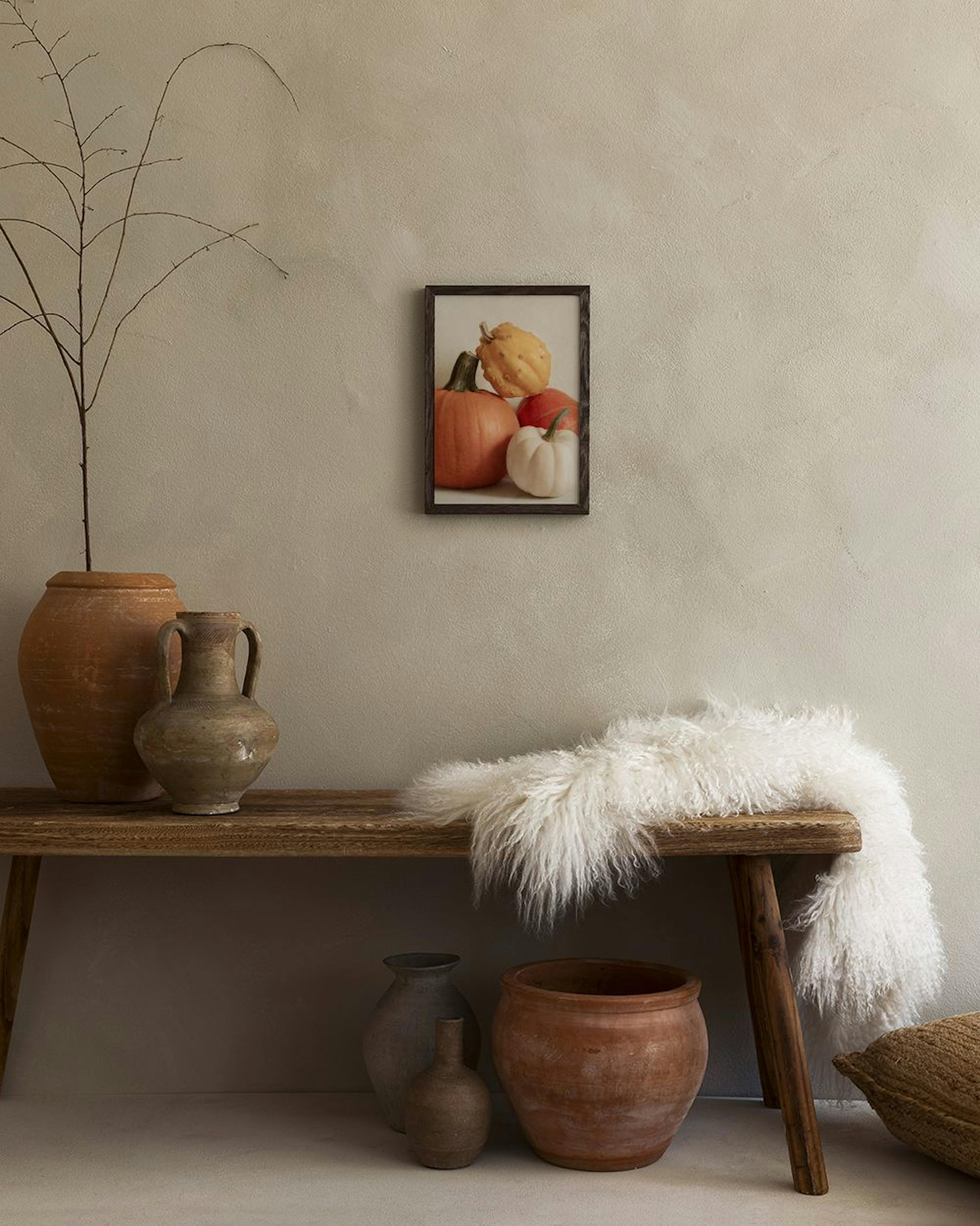 Affiche avec des citrouilles orange, blanches et jaunes, exposée sur un mur au-dessus dun banc en bois rustique avec des pots en