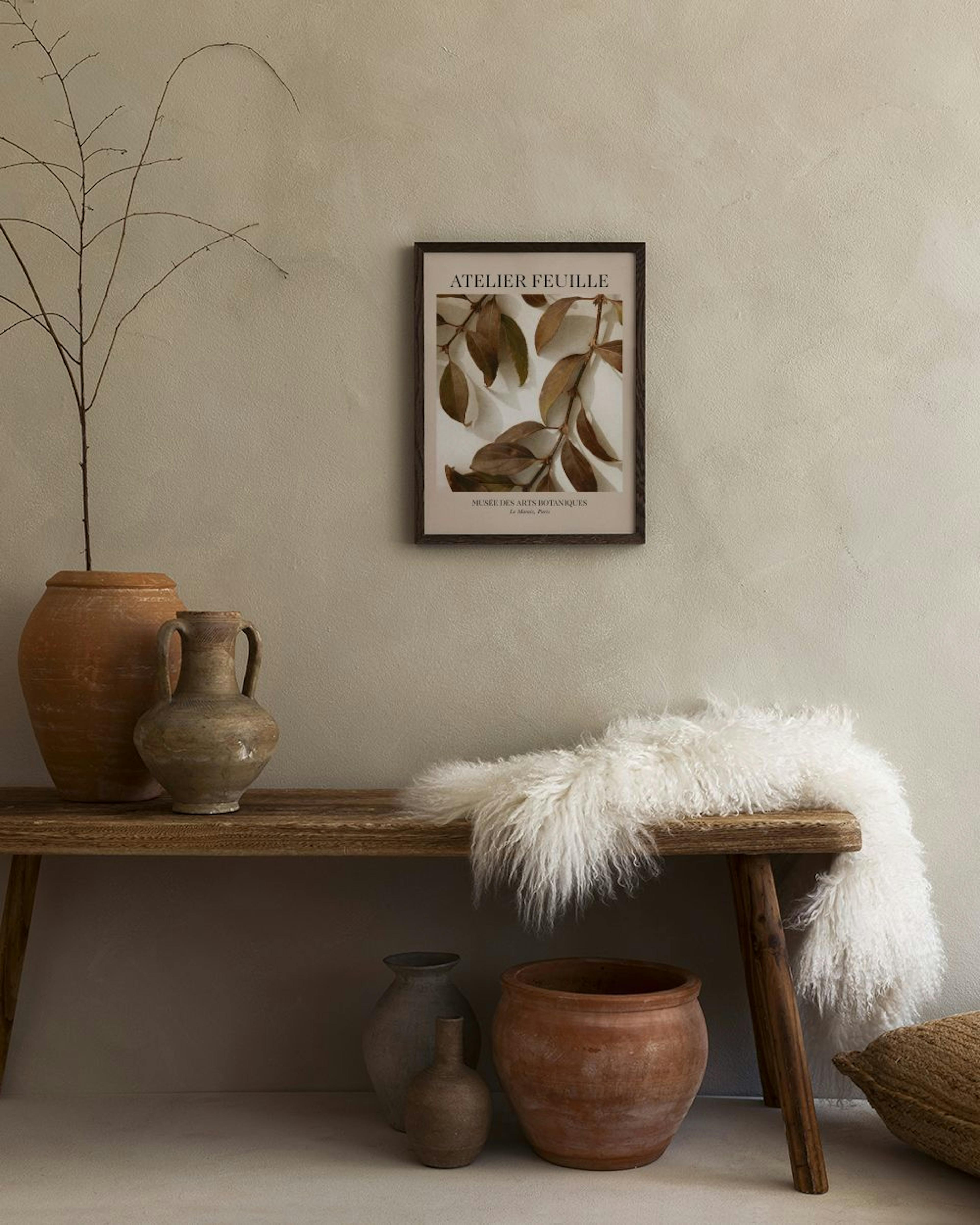 Affiche botanique Atelier Feuille avec branches de feuilles marron, suspendue au-dessus dun banc en bois avec vase et poterie.