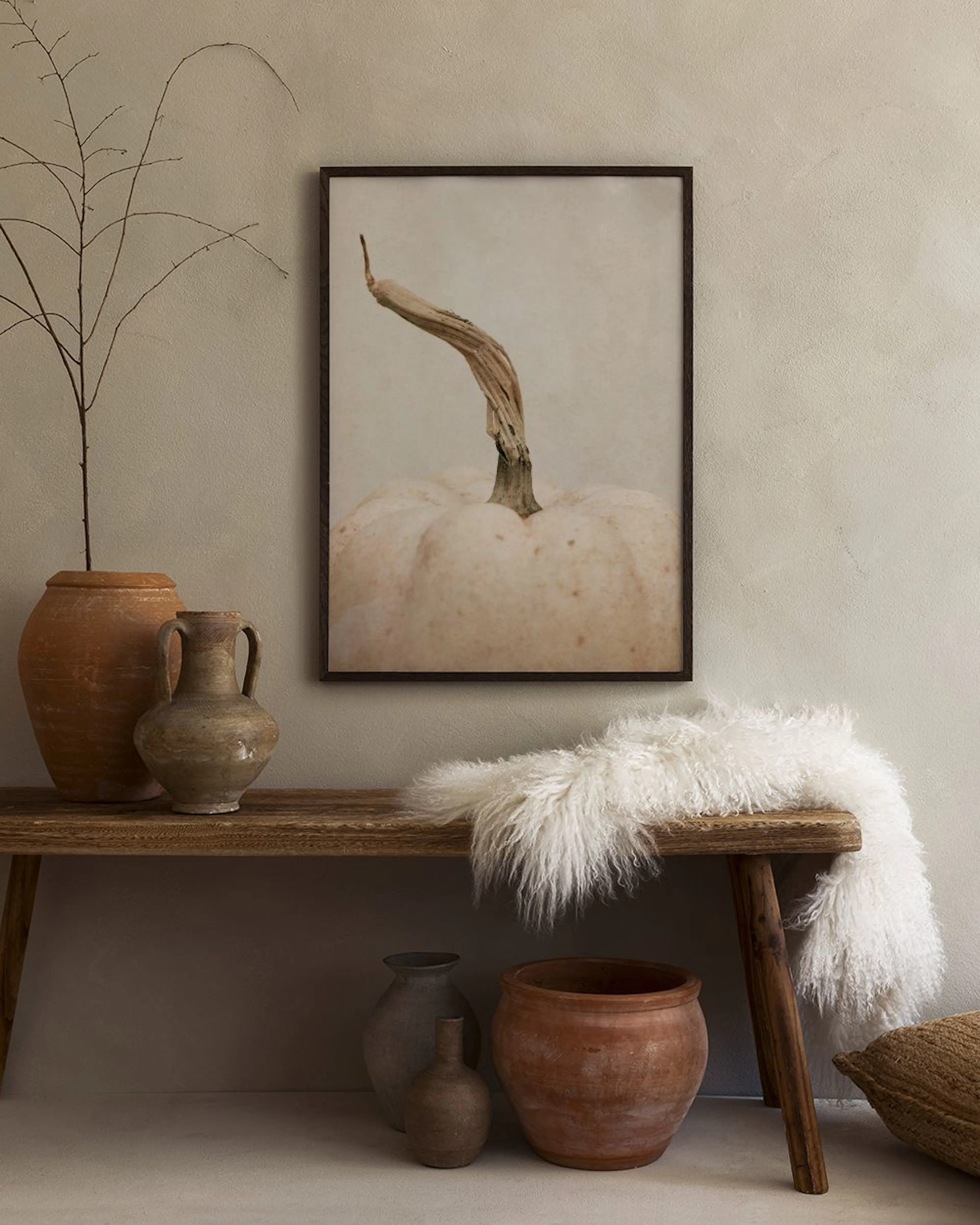 Poster van een witte pompoen met bruine steel, hangend boven een houten bankje met aardewerken potten en een wit kleed.