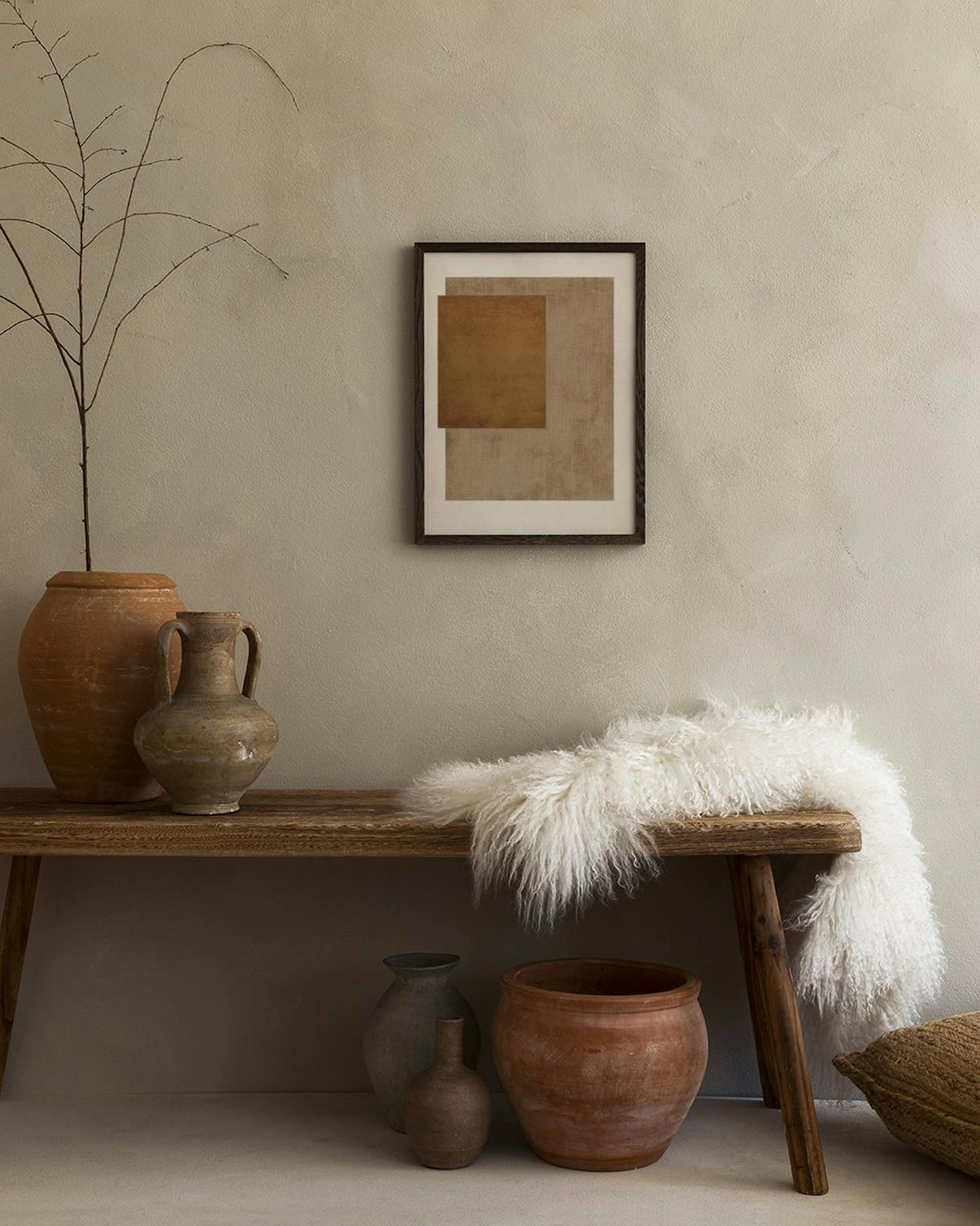 Affiche abstraite de formes rectangulaires texturées marron et beige, exposée au-dessus dun banc en bois avec des poteries.