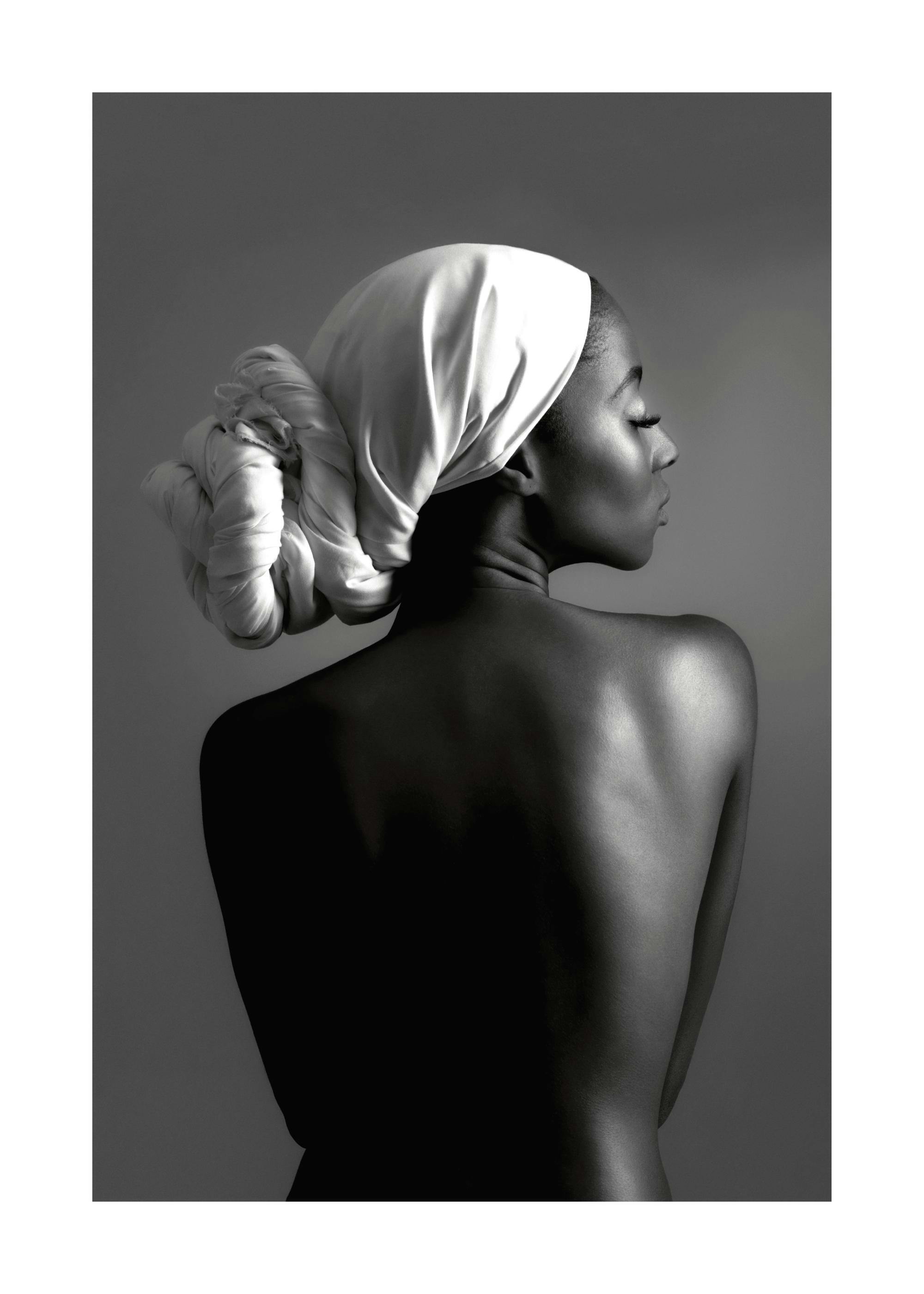 Black and white photograph of a woman with a white scarf wrapped around her hair, seen from behind.