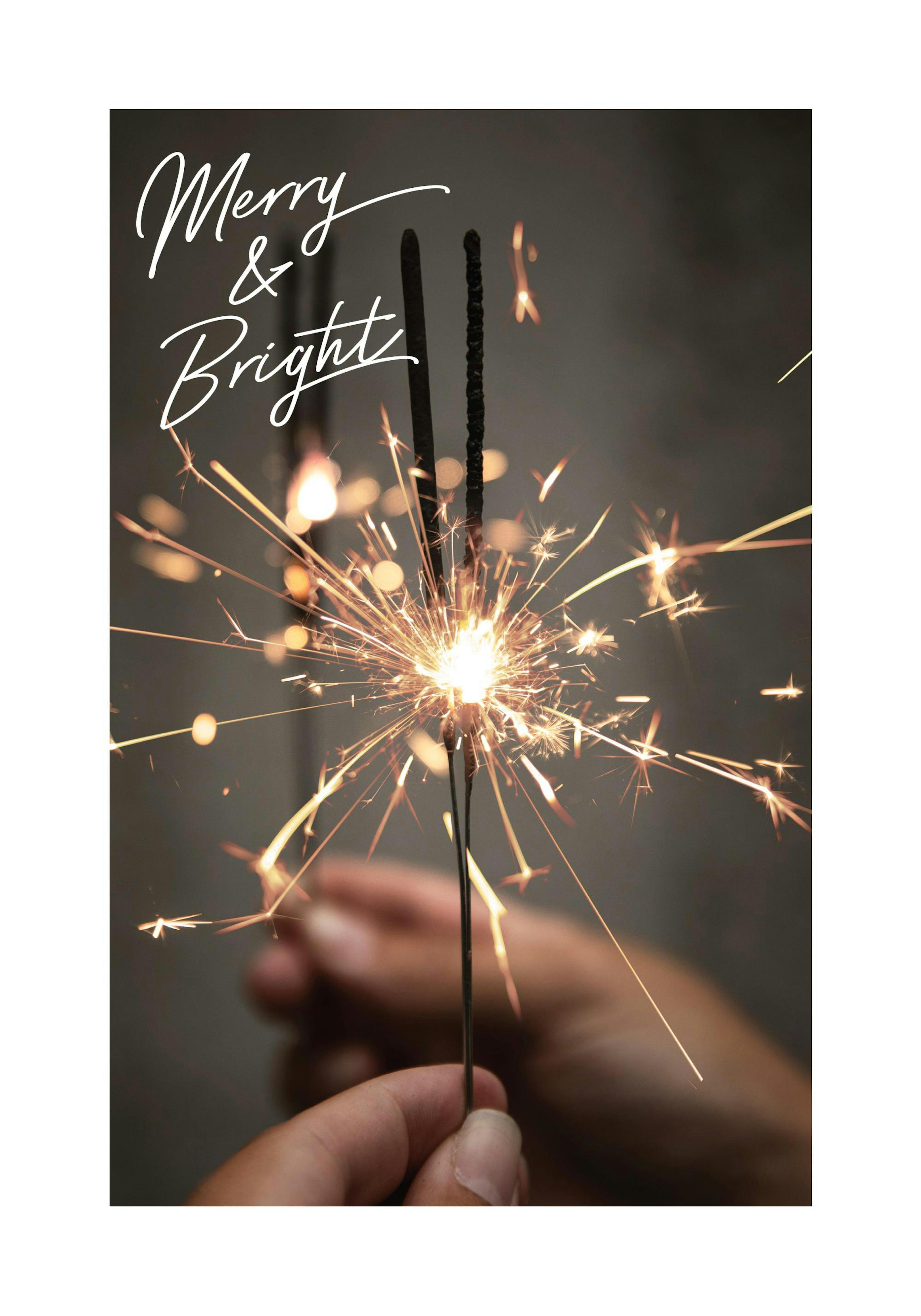 Fotografi av en hand som håller en tänd tomtebloss med gnistor, texten Merry & Bright i vitt upptill. Juldekoration.
