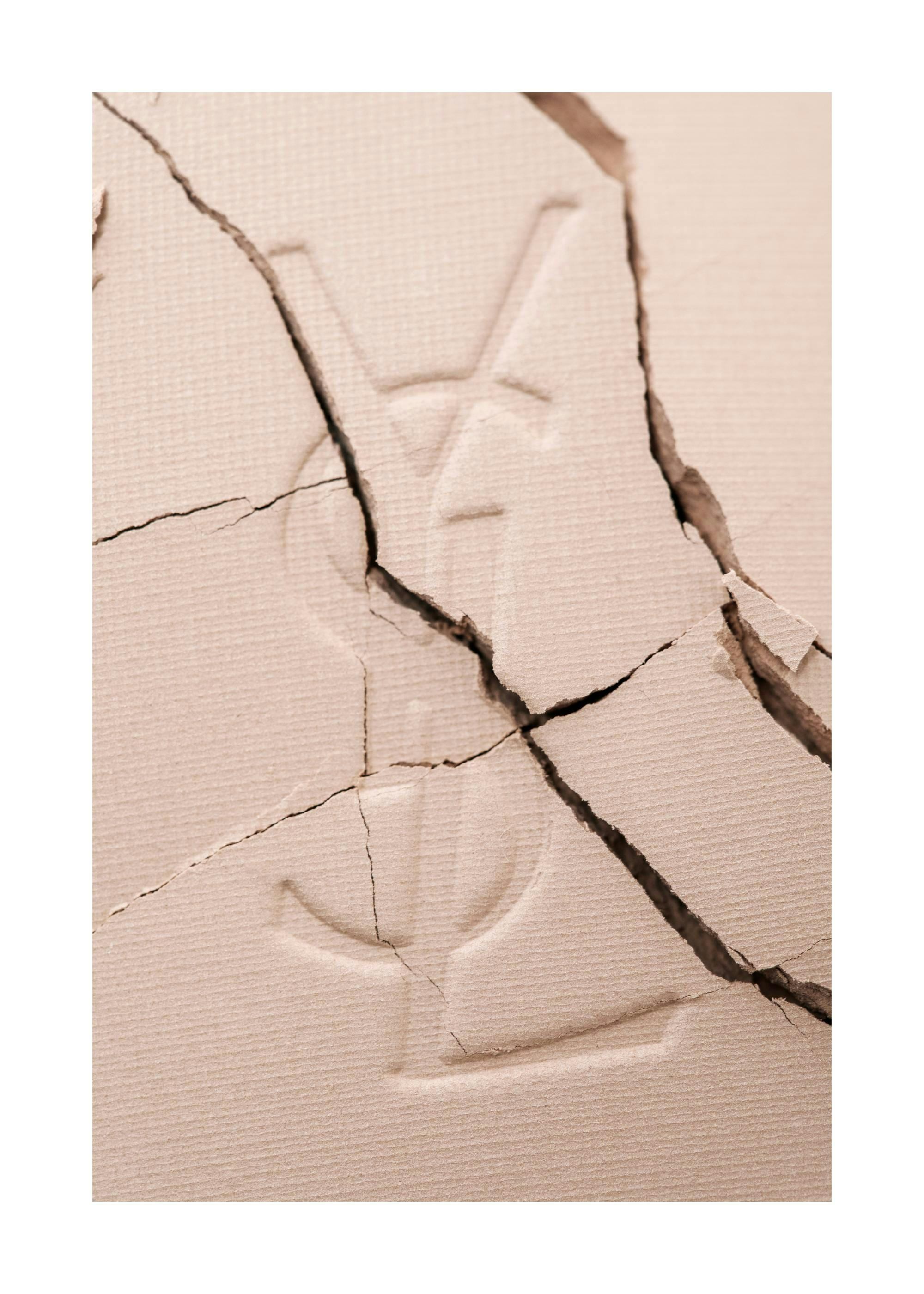 Affiche photographie gros plan dune poudre fissurée avec le logo YSL, teintes beiges, motif exclusif