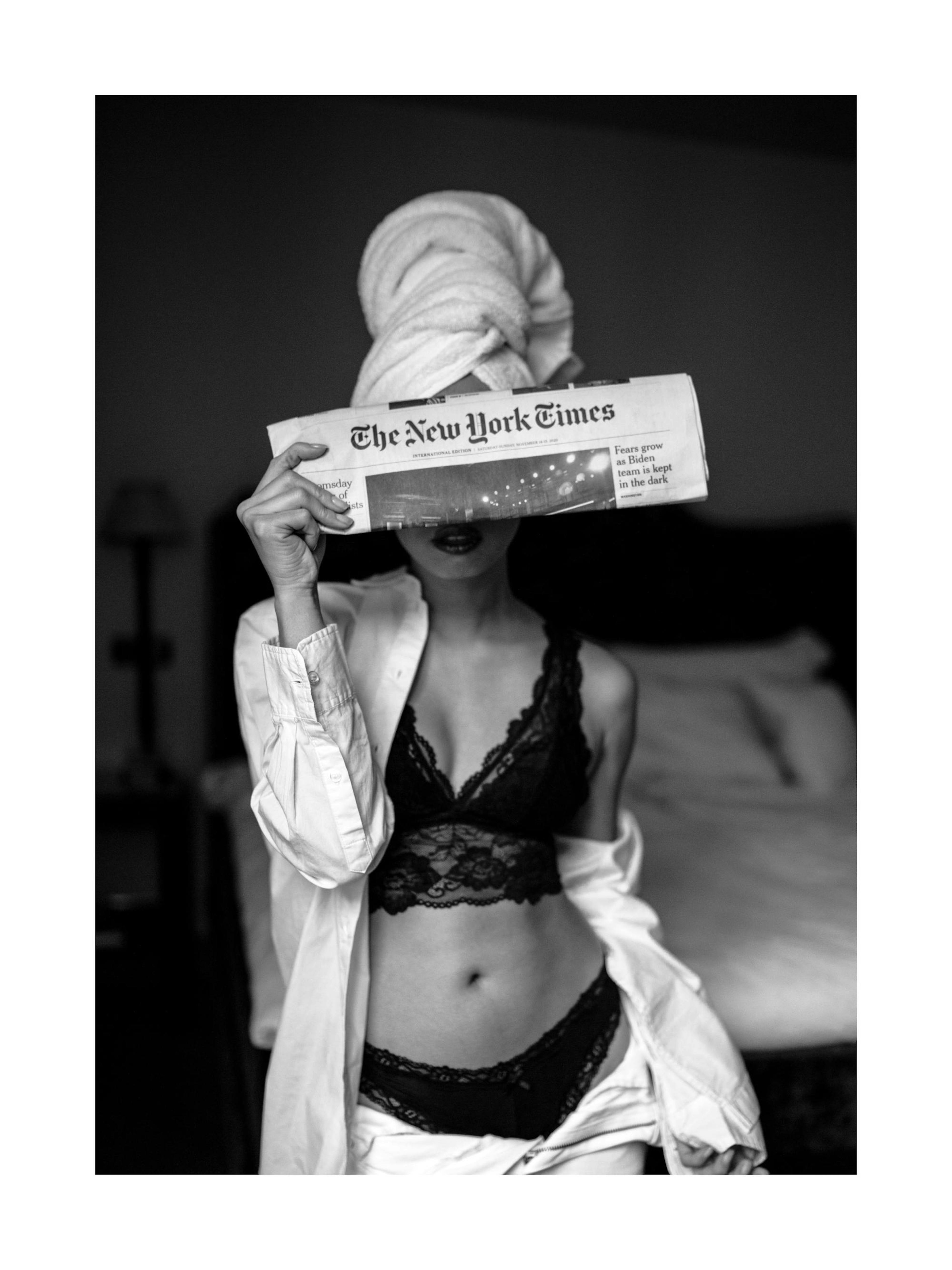 Black and white print of a woman in lingerie and a towel, holding a newspaper over her face. Modern poster.