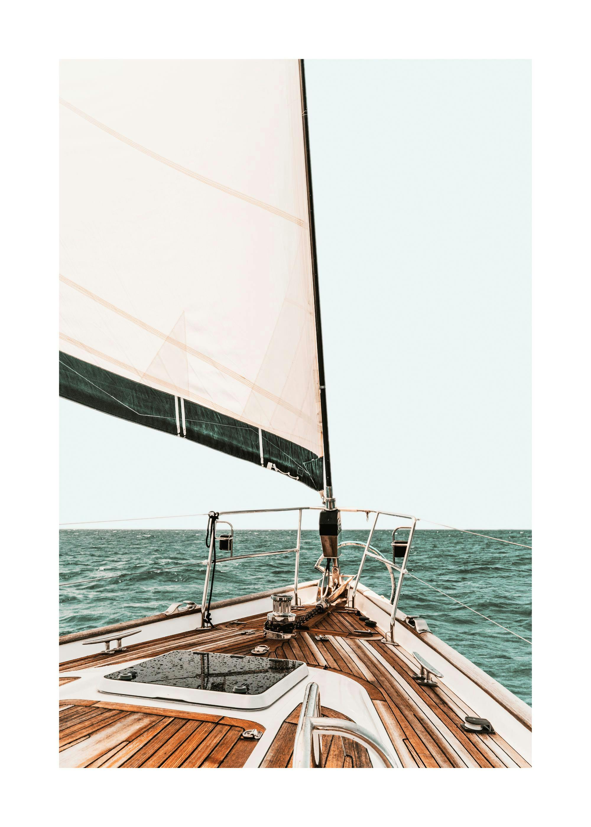 Photograph of the front of a sailboat with a white sail and blue ocean background. Nautical print.