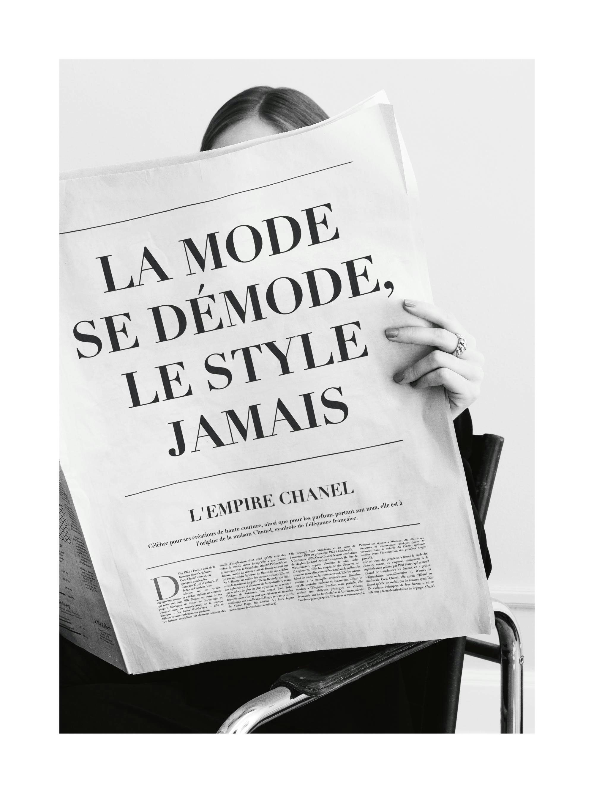 Svartvitt fotografi av en kvinna som läser en tidning med rubriker om mode och Chanel, elegant fotokonst.