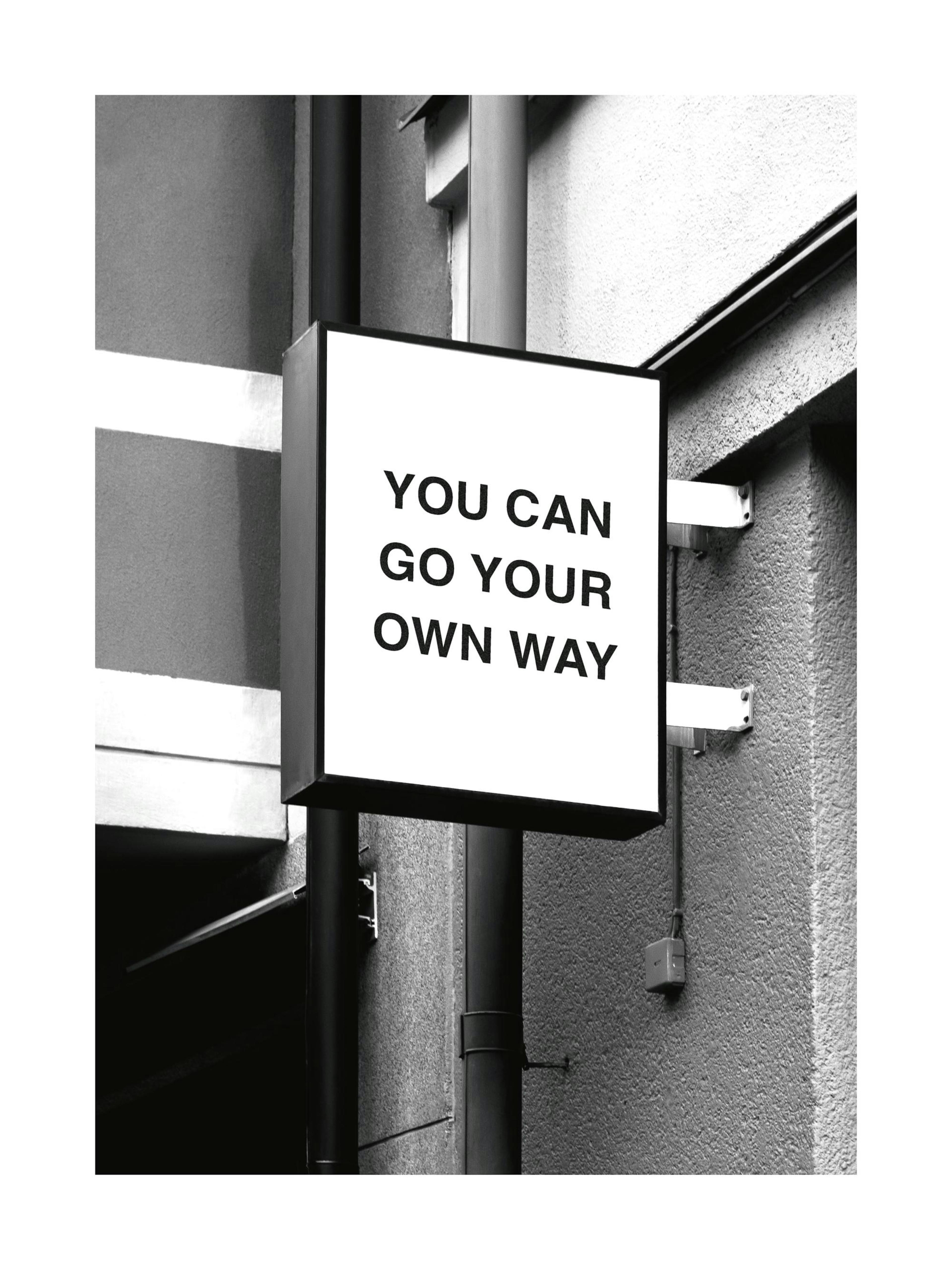 Póster monocromático con un cartel cuadrado que dice YOU CAN GO YOUR OWN WAY en la fachada de un edificio.