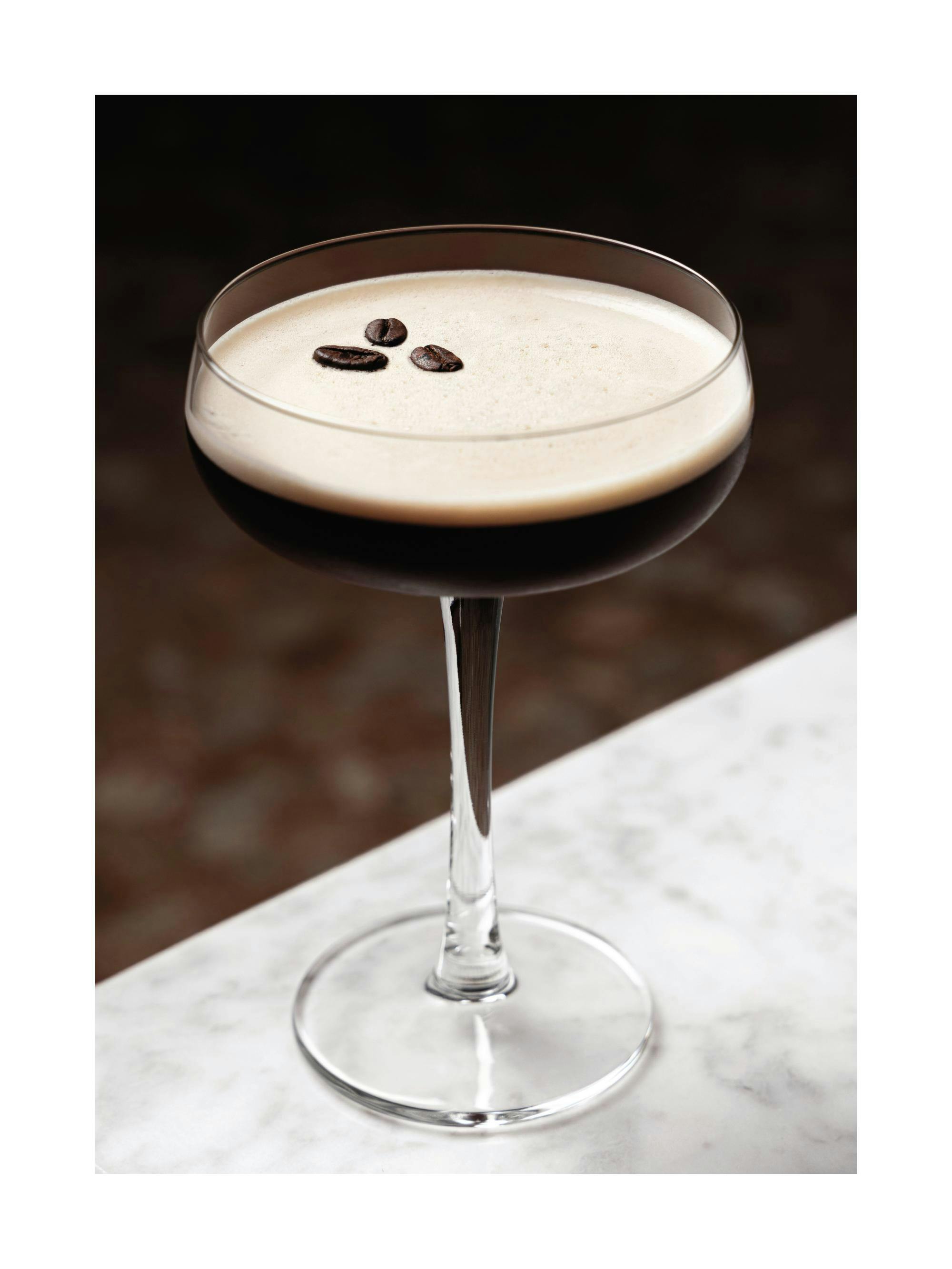 Kaffedrink i glas med tre kaffebönor på toppen, placerad på ett vitt marmorbord. Perfekt för köket.