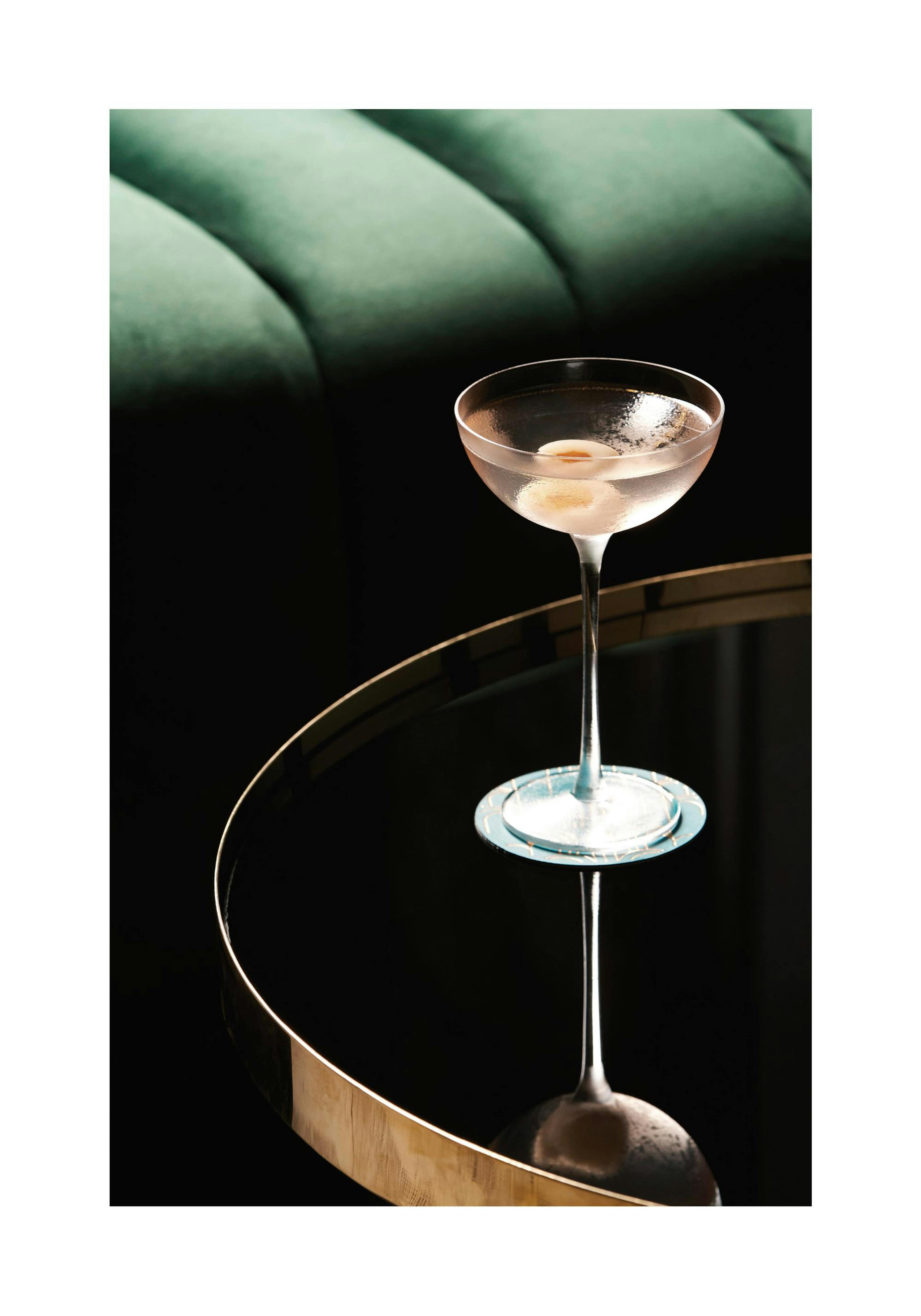 Drink with olive in glass on round table with green velvet sofa, a print poster.