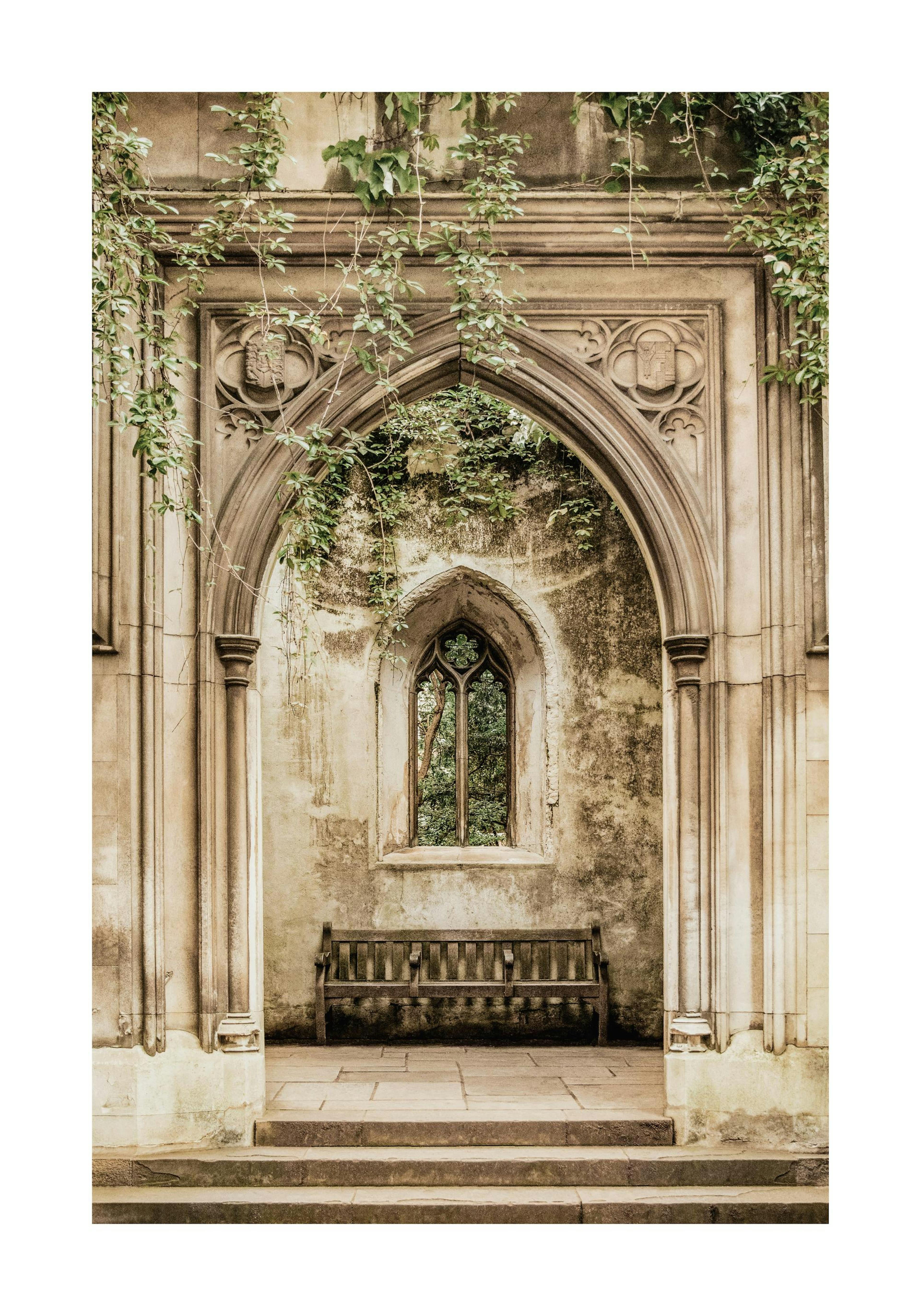 A print of a Gothic stone archway with a bench and ivy, on a textured wall in an art studio.