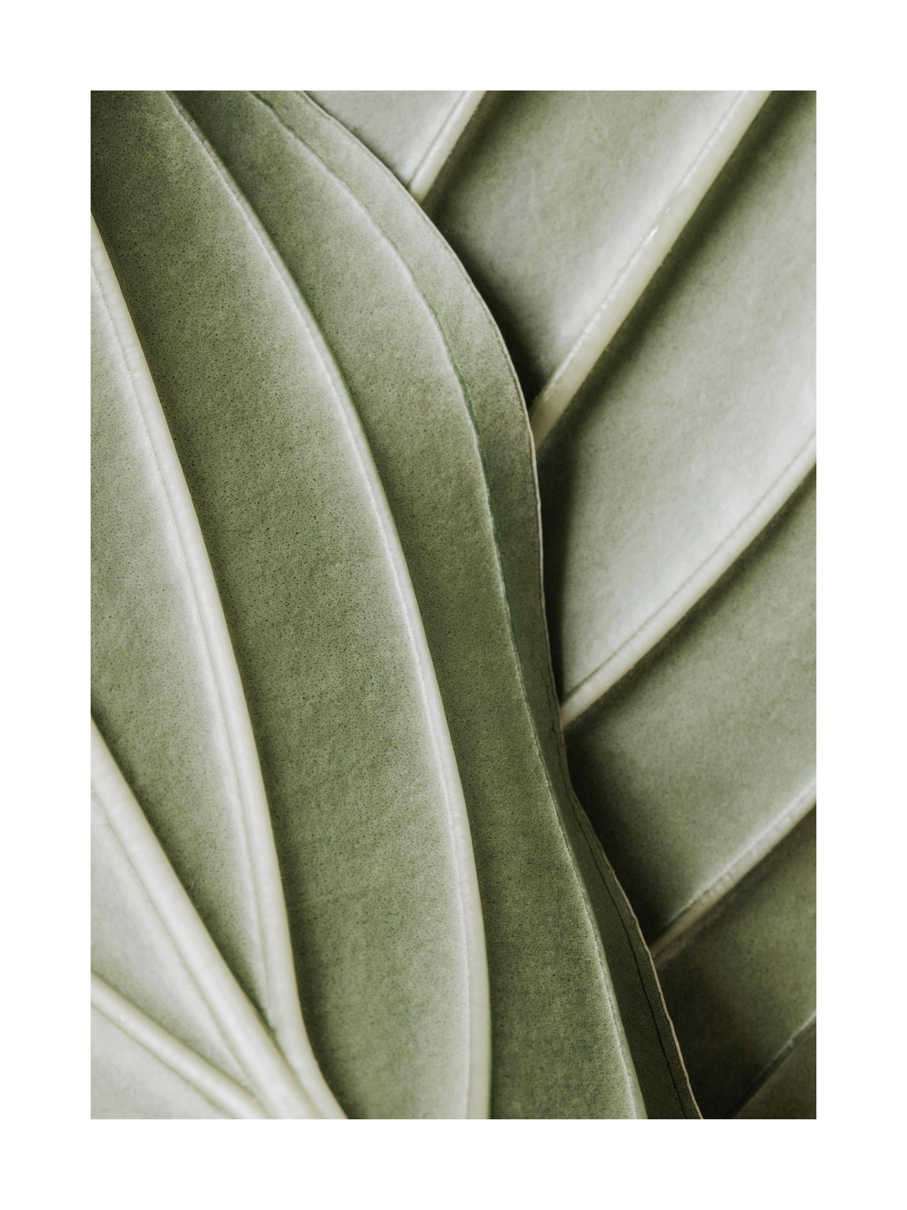 A green leaf print hanging on a textured beige wall, above a wooden stool with books and a white sculpture.