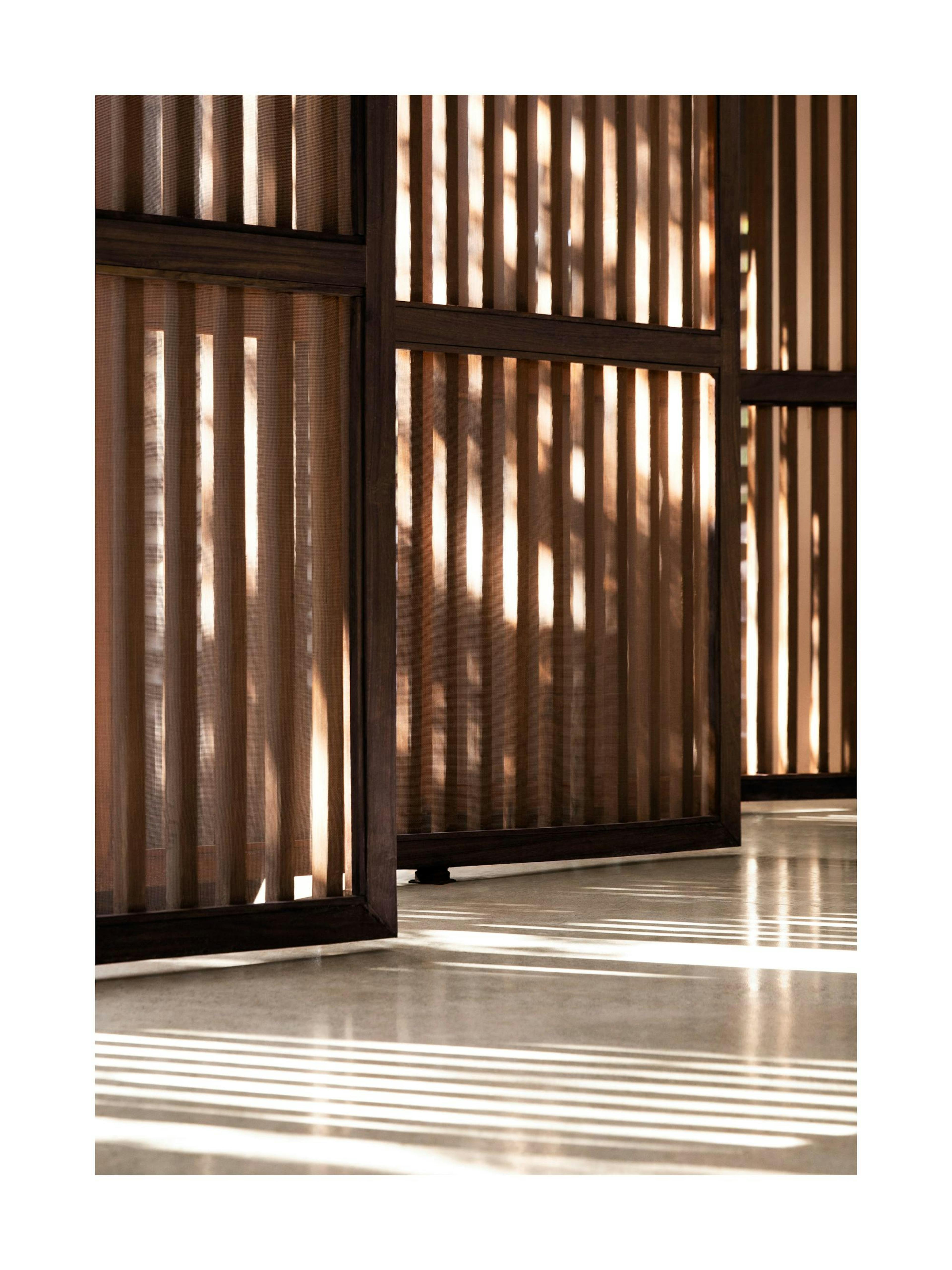 Póster de reflejos de luz solar en un panel de pared de madera, creando rayas de sombra en el suelo.