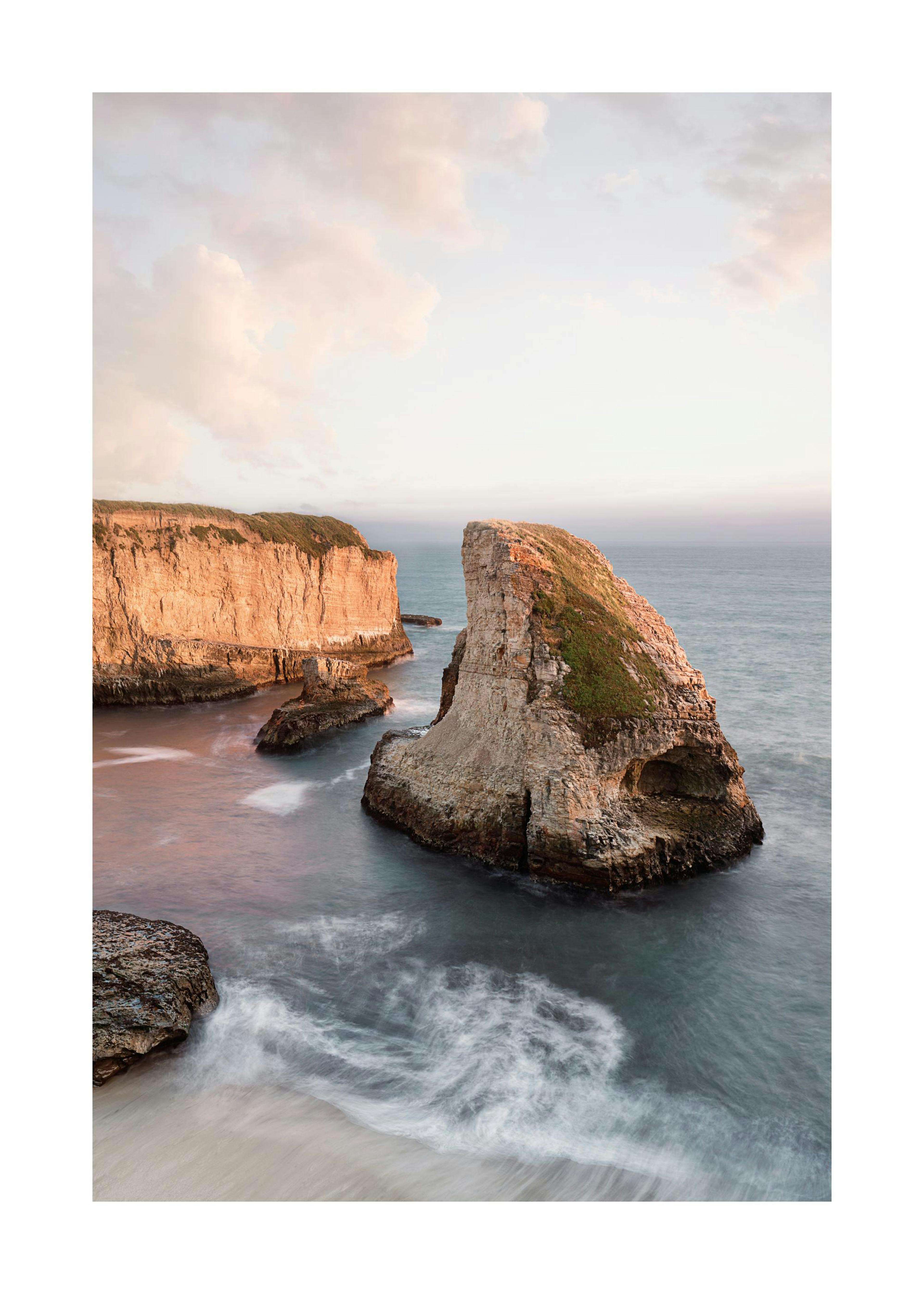 Plakat klifu Shark Fin Cove, z formacjami skalnymi i spokojnymi wodami oceanu pod pastelowym niebem.