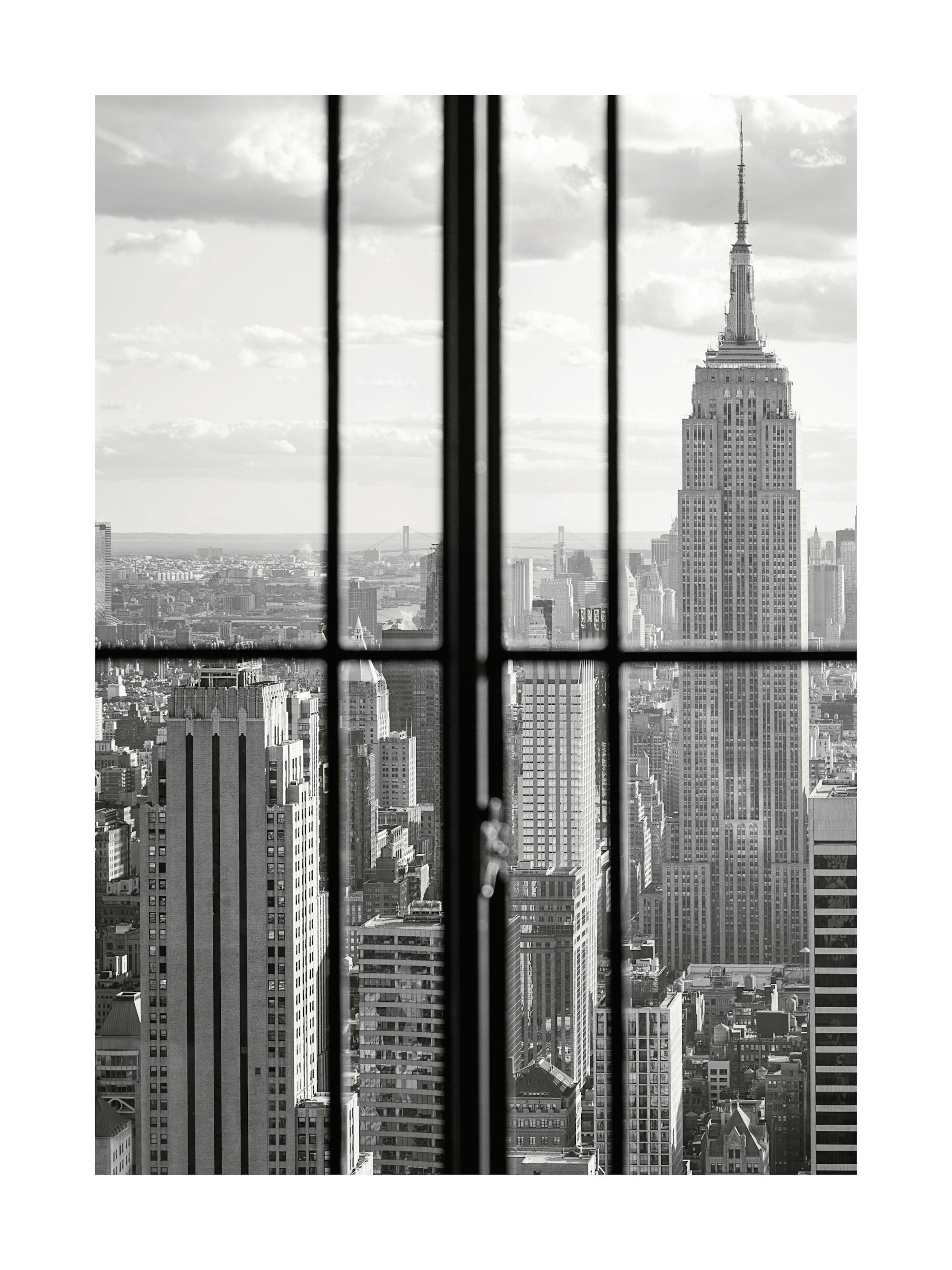 Mustavalkoinen valokuva Manhattanin kaupunkinäkymästä ikkunan läpi, Empire State Building näkyvissä.