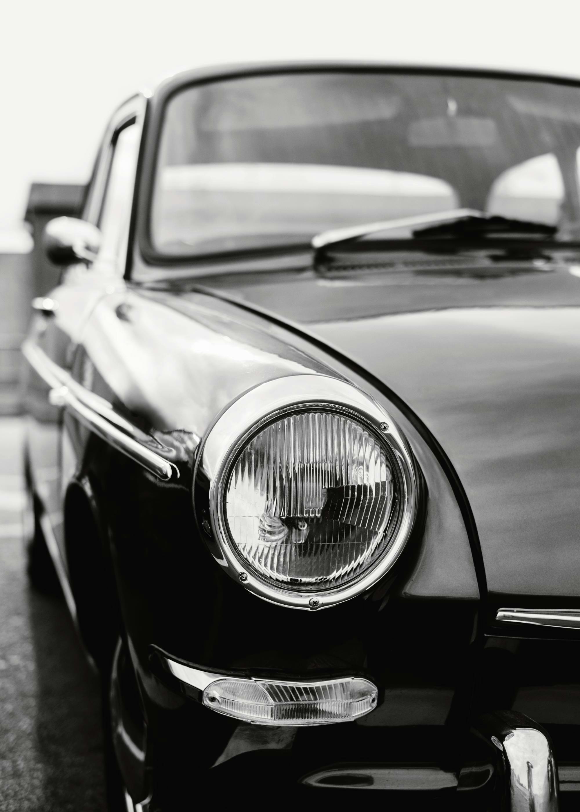 Black and white photograph of a classic cars front, with the headlight and chrome details in sharp focus.