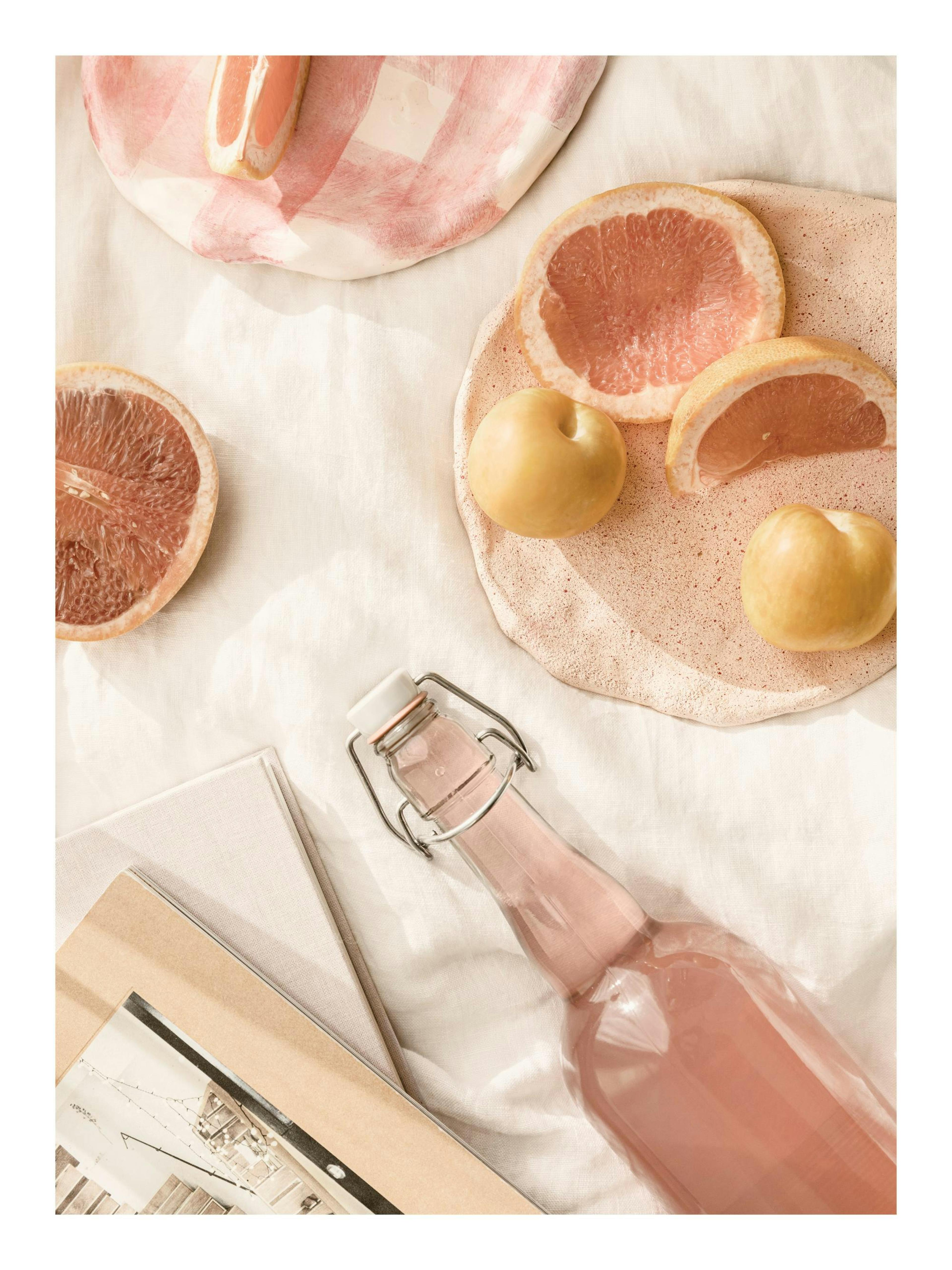 Fotografi af lyserød picnic med grapefrugt, æbler og limonade på beige tæppe