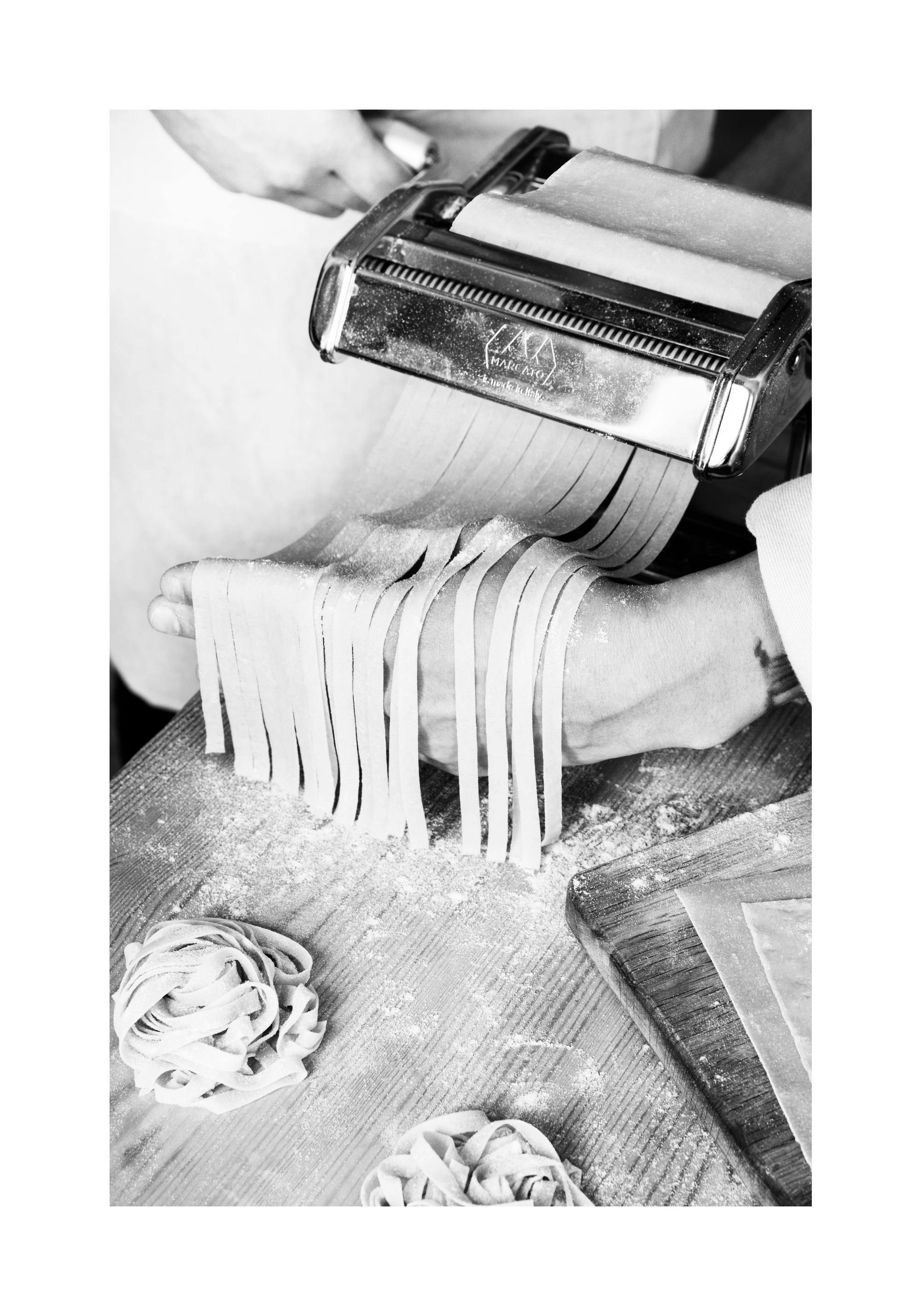 Svartvitt fotografi av en person som gör färsk pasta med pastamaskin. Köksinredning.