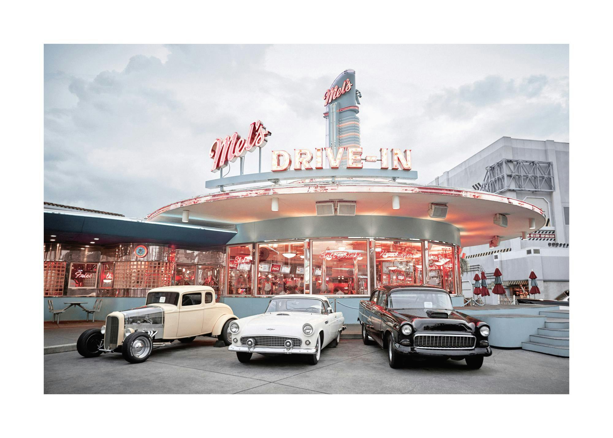 Foto eines Drive-in-Diners mit leuchtender Neonreklame und drei klassischen Autos davor. Retro-Poster.