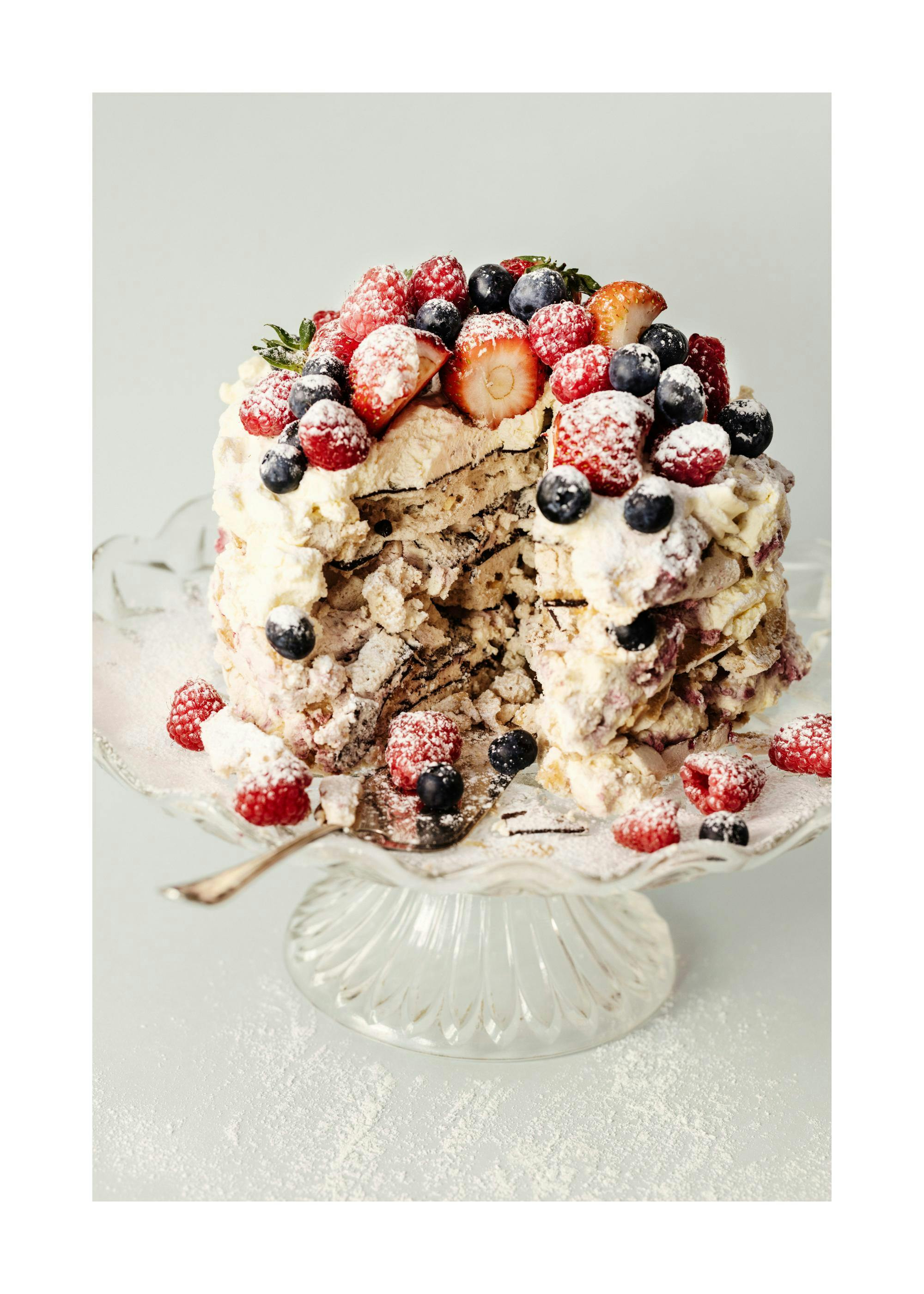 Pastel de bayas parcialmente comido, cubierto de frambuesas, arándanos y fresas, espolvoreado con azúcar glas.