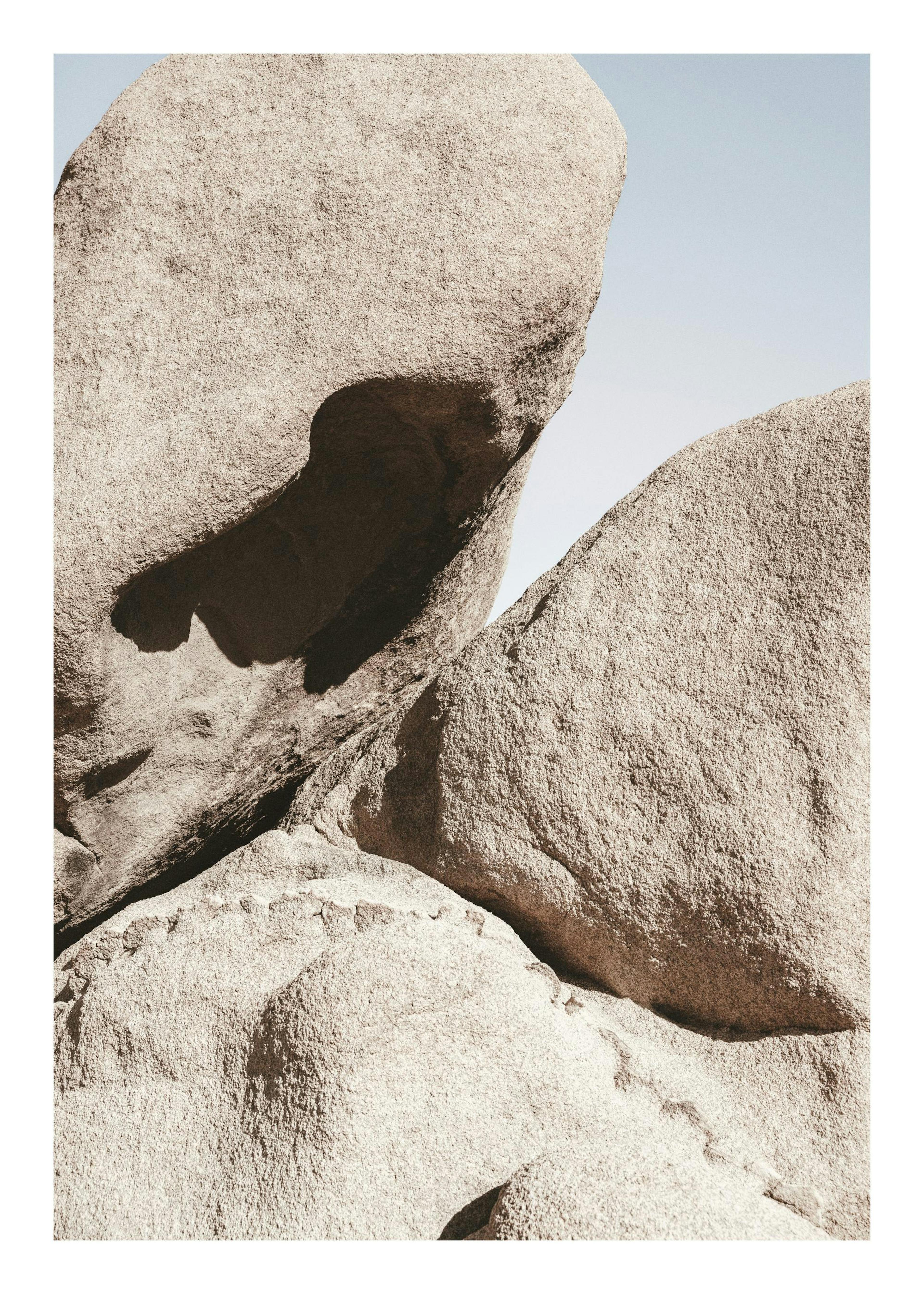 Póster de rocas beige y grises, con textura rugosa y sombras profundas, bajo un cielo claro. Naturaleza audaz.