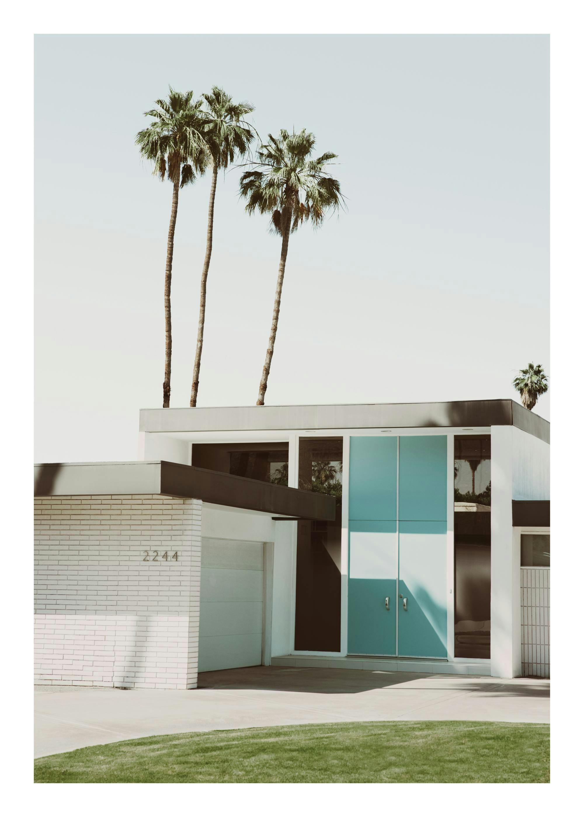 Póster de villa moderna de mediados de siglo, casa de ladrillo blanco con puerta de garaje azul y palmeras.