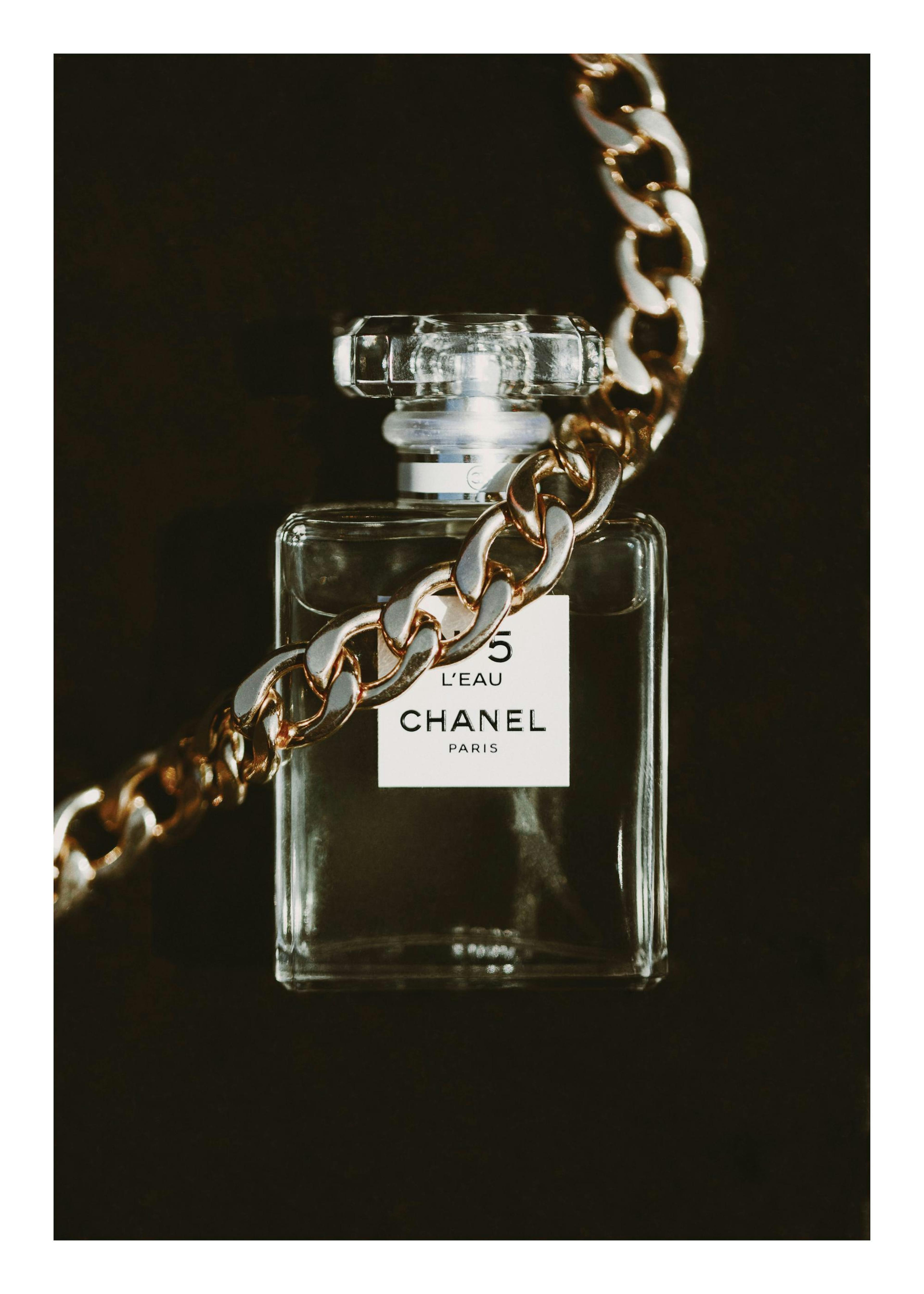 Plakat z butelką perfum Chanel No. 5 LEau z złotym łańcuszkiem na czarnym tle, dekoracja ścienna.