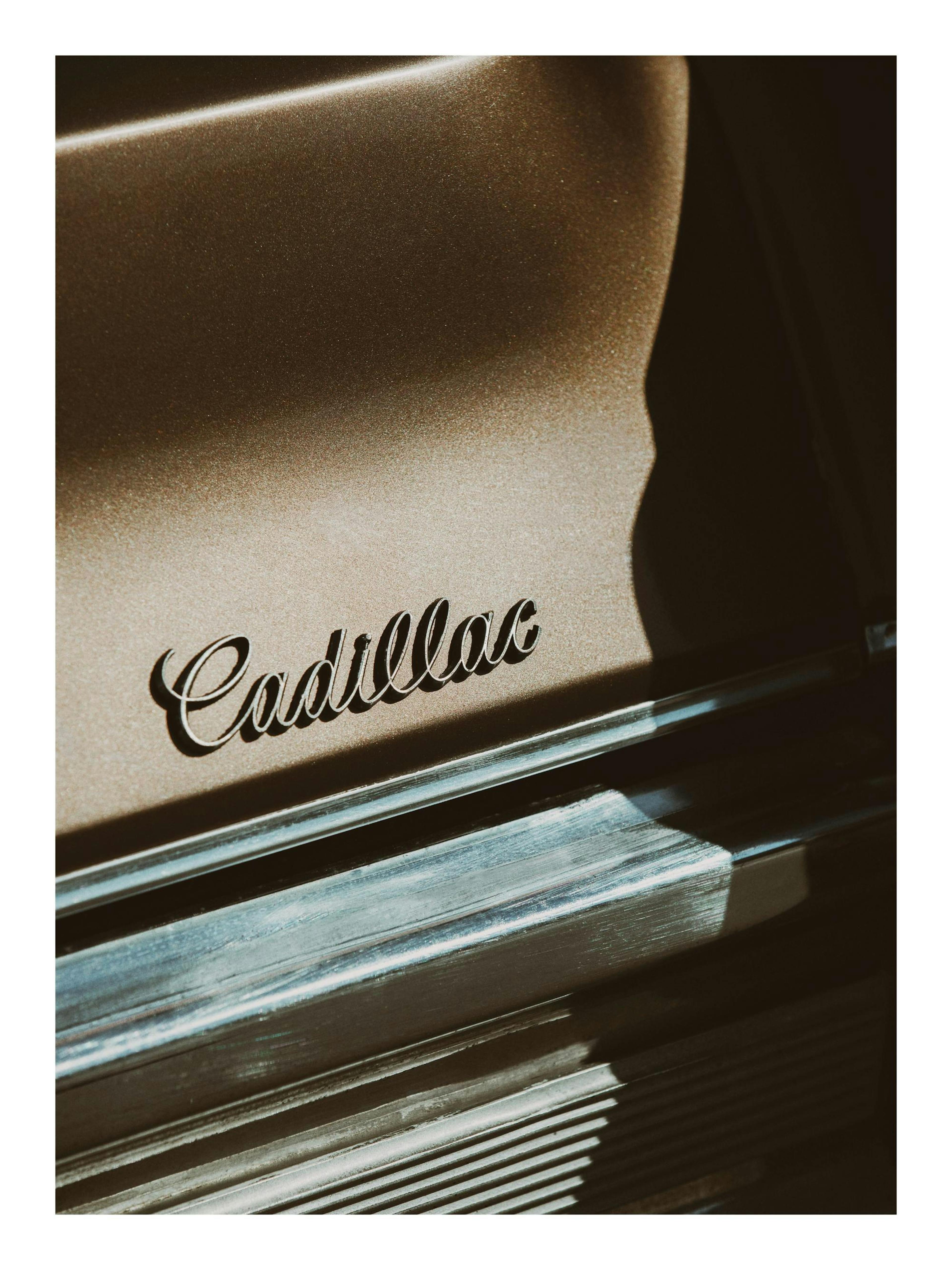 Primer plano de un clásico Cadillac marrón con el nombre en cursiva y detalles cromados brillantes, estilo vintage.