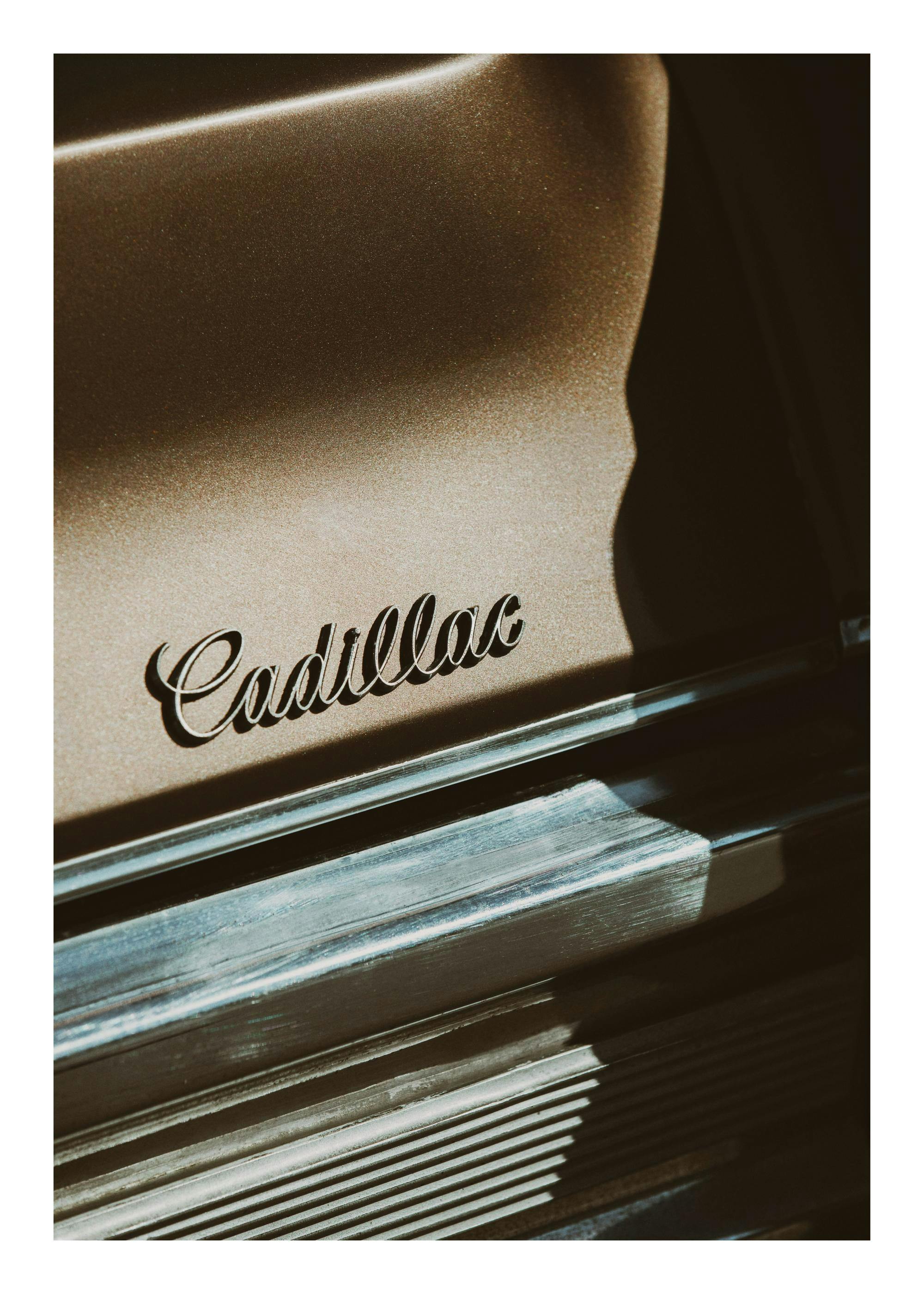 Primer plano de un clásico Cadillac marrón con el nombre en cursiva y detalles cromados brillantes, estilo vintage.